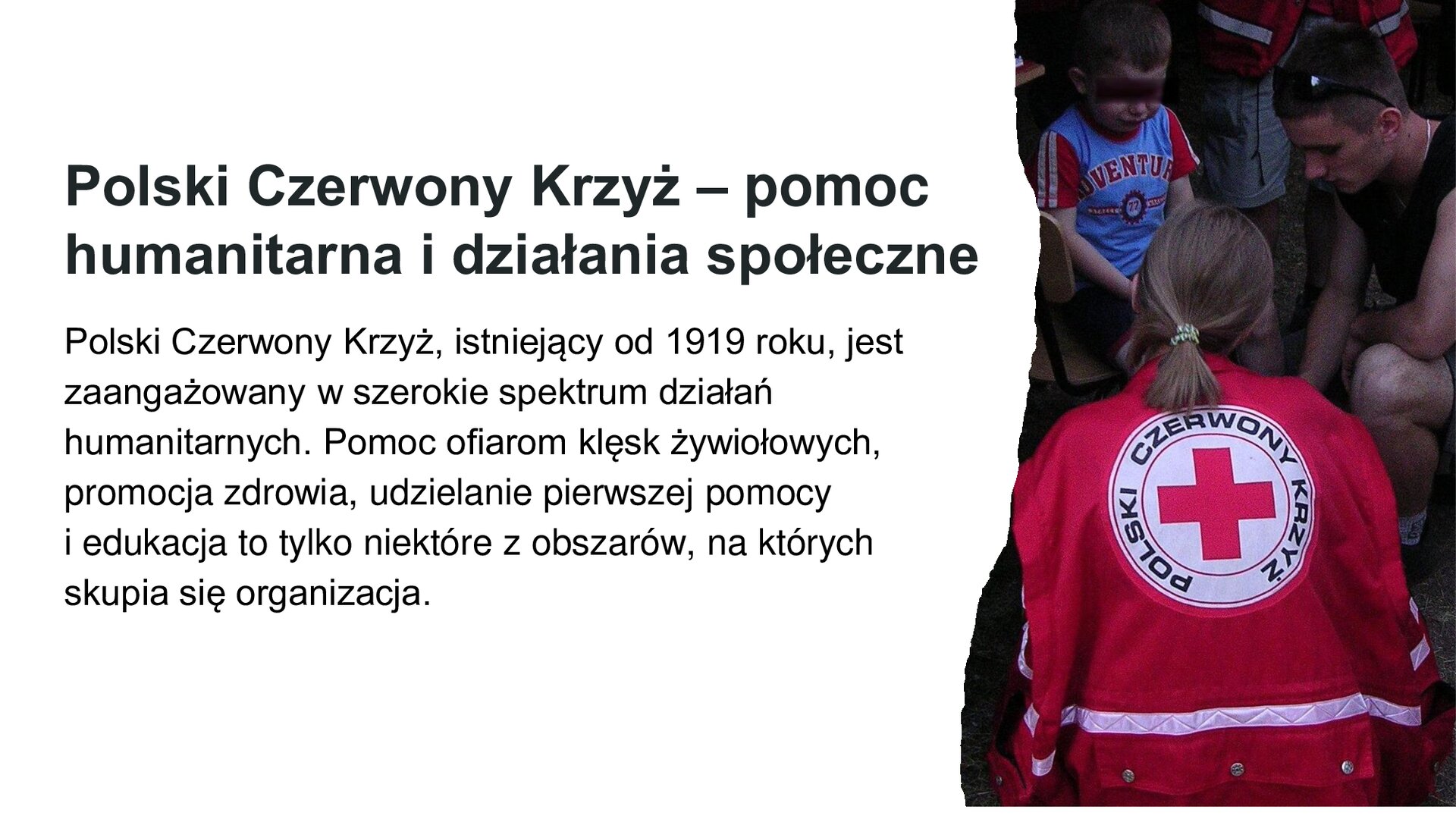 Biały slajd. Z lewej strony tekst: „Polski Czerwony Krzyż - pomoc humanitarna i działania społeczne. Polski Czerwony Krzyż, istniejący od 1919 roku, jest zaangażowany w szerokie spektrum działań humanitarnych. Pomoc ofiarom klęsk żywiołowych, promocja zdrowia, udzielanie pierwszej pomocy i edukacja to tylko niektóre z obszarów, na których skupia się organizacja”. Z prawej strony zdjęcie kobiety odwróconej tyłem do widza, która ubrana jest w czerwoną kurtką, na której znajduje się białe logo Czerwonego Krzyża. Kuca przed małym chłopcem i dorosłym.