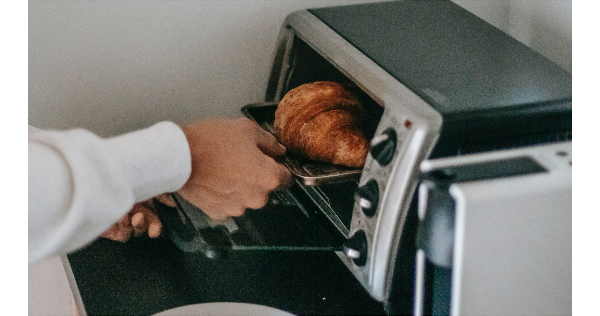Zdjęcie przedstawia rękę osoby wkładającej rogalik do piekarnika.