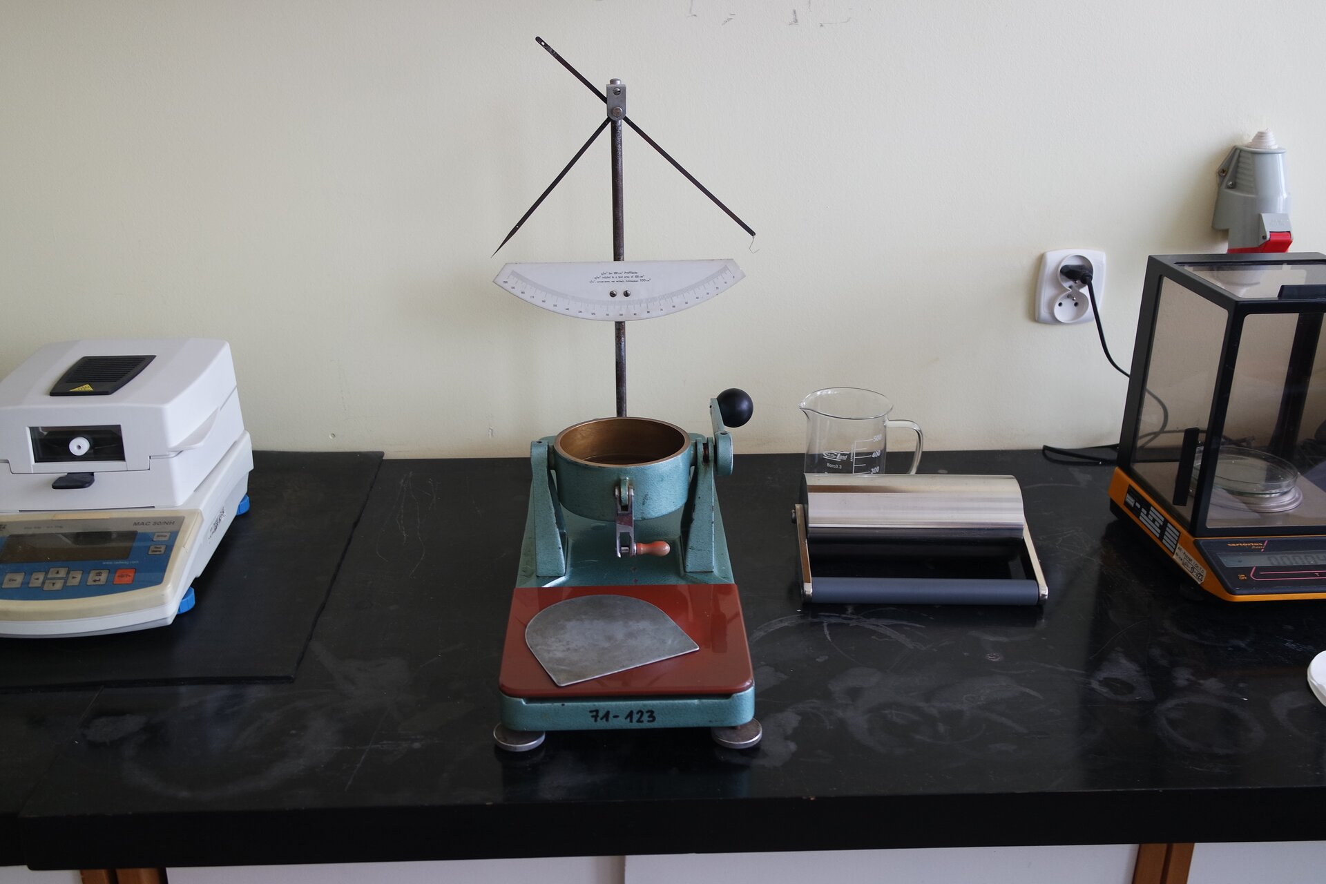 Na zdjęciu przedstawiono aparat Cobba. Urządzenie składa się z metalowego blatu osadzonego na nóżkach antypoślizgowych. Na blacie znajduje się cylinder wyposażony w gałkę i korbkę. Za cylindrem znajduje się pionowy element zakończony półkrzyżem oraz półokrągła tabliczka z podziałką.