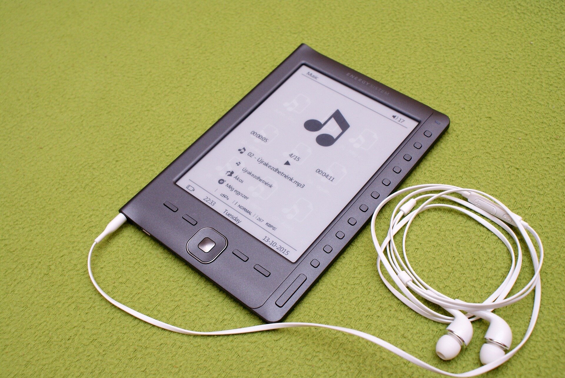 Na ilustracji znajduje się cienki panel z dużym ekranem, na którym wyświetlony jest program do odtwarzania muzyki. Pod ekranem znajduje się taczpad. Po obydwóch jego stronach umiejscowione zostały po dwa przyciski. Po prawej stronie od ekranu znajduje się rząd małych kwadratowych przycisków - jest ich jedenaście. Pod nimi, w tej samej linii, widać podłużny klawisz. Do urządzenia podłączone są słuchawki douszne.