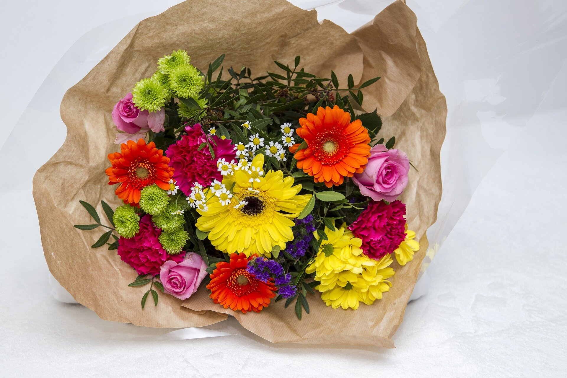 Zdjęcie przedstawia bukiet różnorodnych, różnokolorowych kwiatów, który owinięty jest papierem.