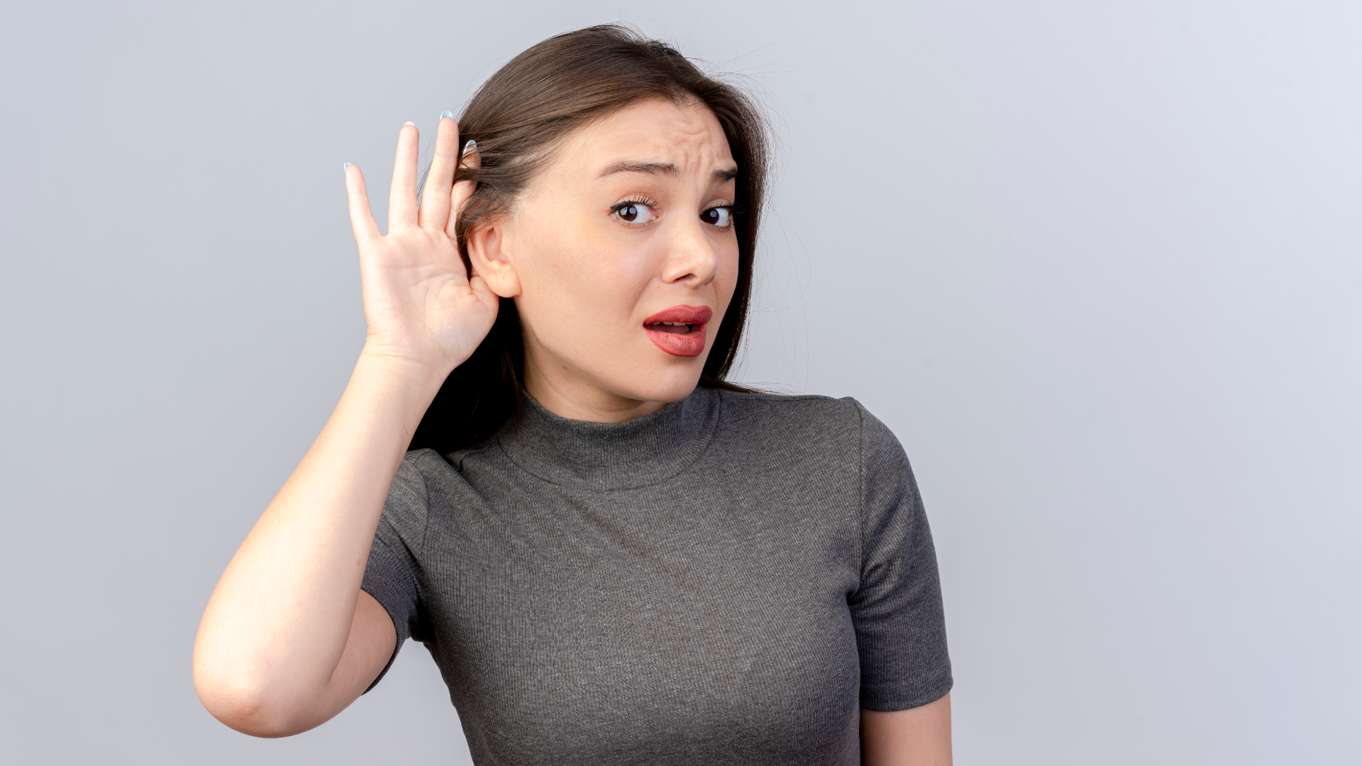 Zdjęcie przedstawia kobietę. Kobieta trzyma otwartą dłoń przy uchu. Kobieta nadstawia ucha, tak jakby czegoś nie dosłyszała lub nie zrozumiała.