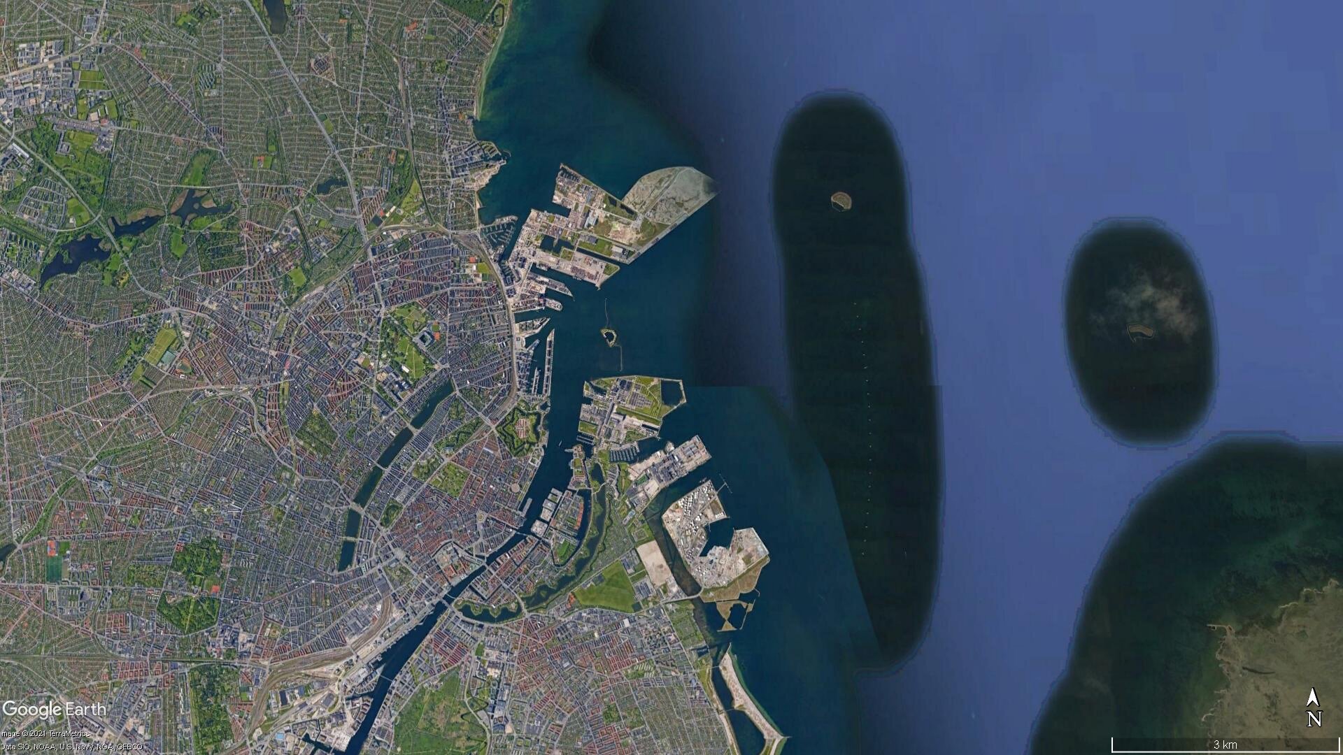 Zdjęcie przedstawia widok satelitarny na port w Kopenhadze. Przy porcie znajduje się ujście rzeki. Wokół niego są zabudowania portu. Miasto jest gęsto zabudowane.
