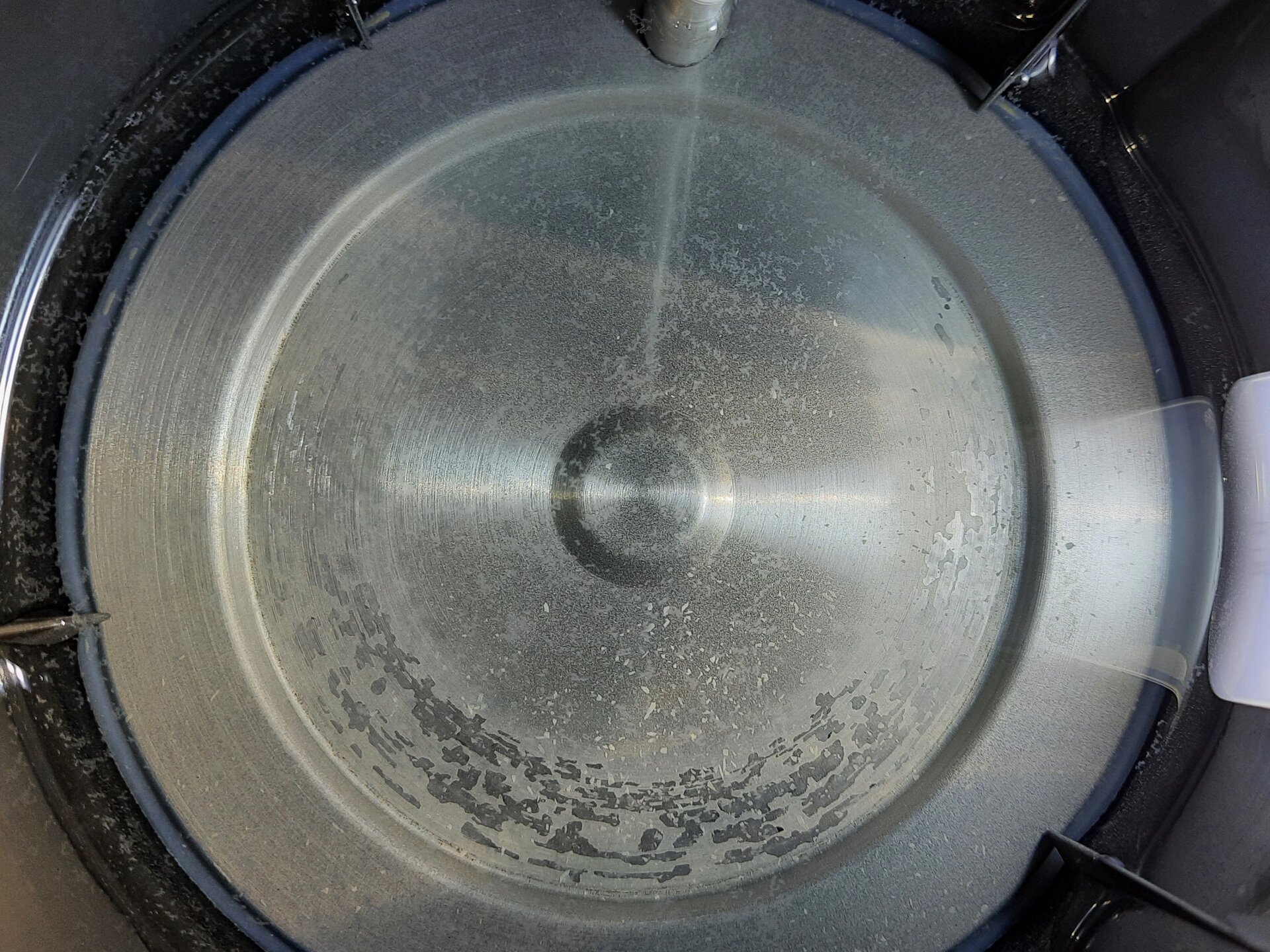 Zdjęcie przedstawia okrągłe metalowe dno czajnika. Na jego powierzchni jest biały nalot. 