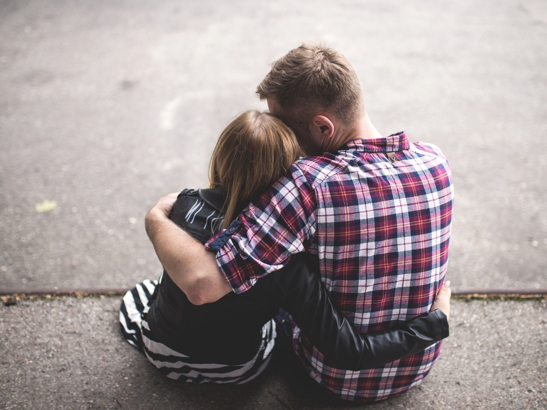 Ilustracja numer trzy. Na zdjęciu chłopak obejmujący dziewczynę. Siedzą. Sfotografowani są od tyłu.