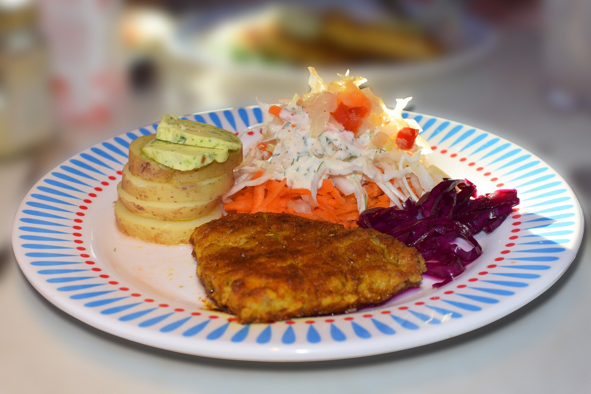 Zdjęcie- biały talerz, na nim kotlet schabowy, puree z ziemniaków, surówki z kapusty, marchewki, buraczków.