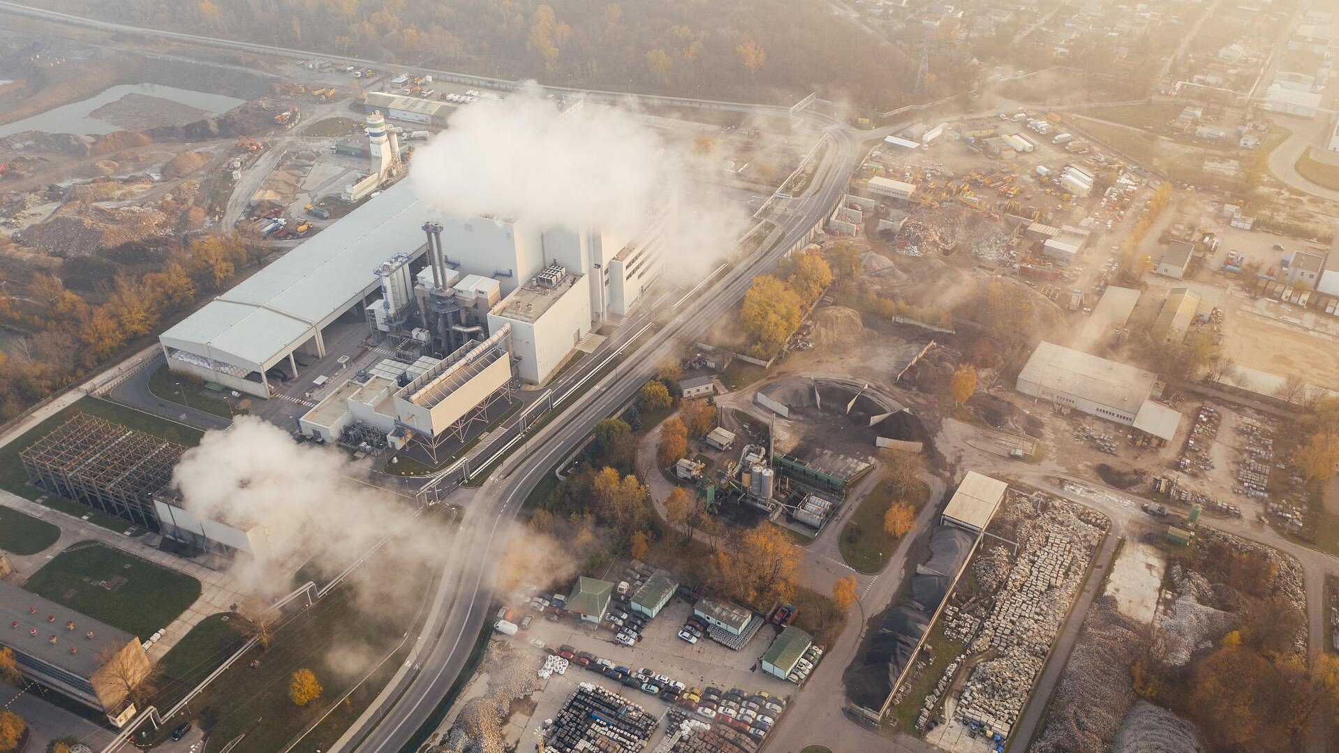 Zdjęcie przedstawia widok z góry na fabrykę znad której unosi się dym.