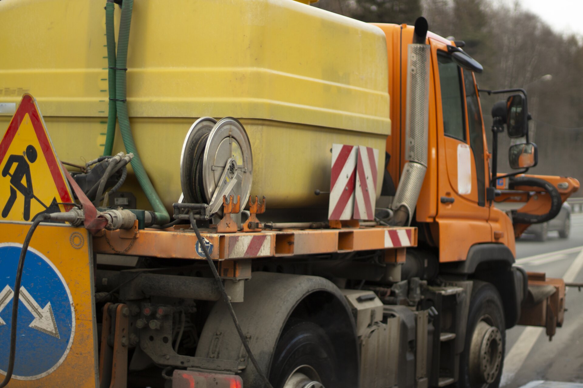 Zdjęcie przedstawia skarpiarkę nadpoziomową. Widoczny jest pojazd, w ujęciu z ukosa, z tyłu. W przedniej części widoczna jest kabina kierowcy, za którą znajduje się platforma. Na platformie widoczny jest duży, żółty zbiornik oraz kołowrotek, liny, zaczepy oraz znaki informujące o pracach.

Opisy obiektów prezentowanych na grafikach są załączone w treści galerii zdjęć. 