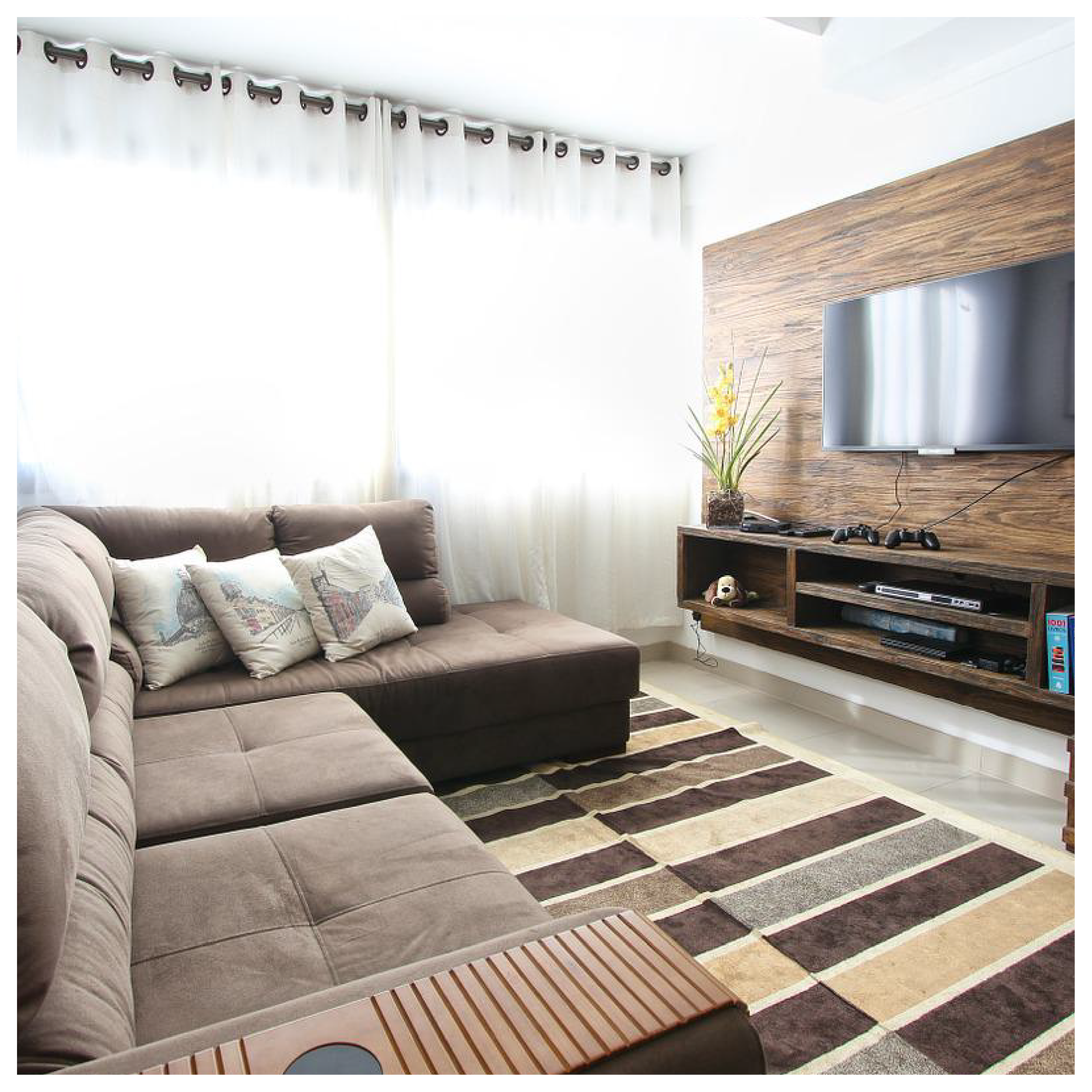 Widoczny jest salon. Na przeciwko dużej sofy wisi telewizor. Na prostopadłej ścianie duże okno. Na środku dywan.