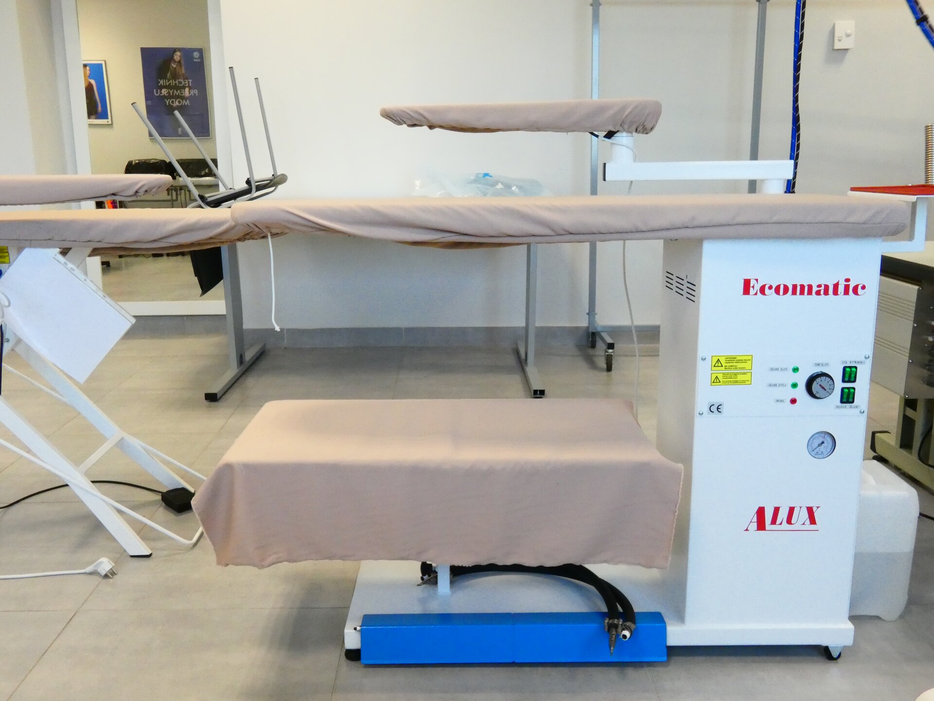 Zdjęcie przedstawia urządzenie składające się z dwóch desek umieszczonych na różnych poziomach jedna nad drugą. Opierają się one na białym klocku, na którym znajdują się różne przyciski. Deski są pokryte bladoróżowym materiałem.