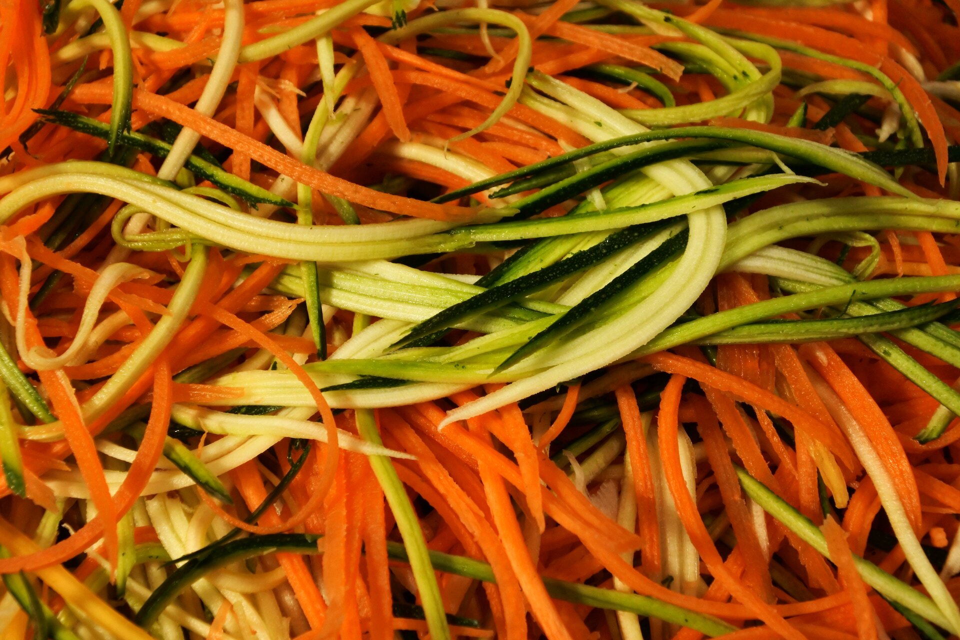 Zdjęcie przedstawia cukinię i marchew pokrojone techniką julienne. Widoczne są cienkie słupki marchwi i cukinii narzucone na siebie.