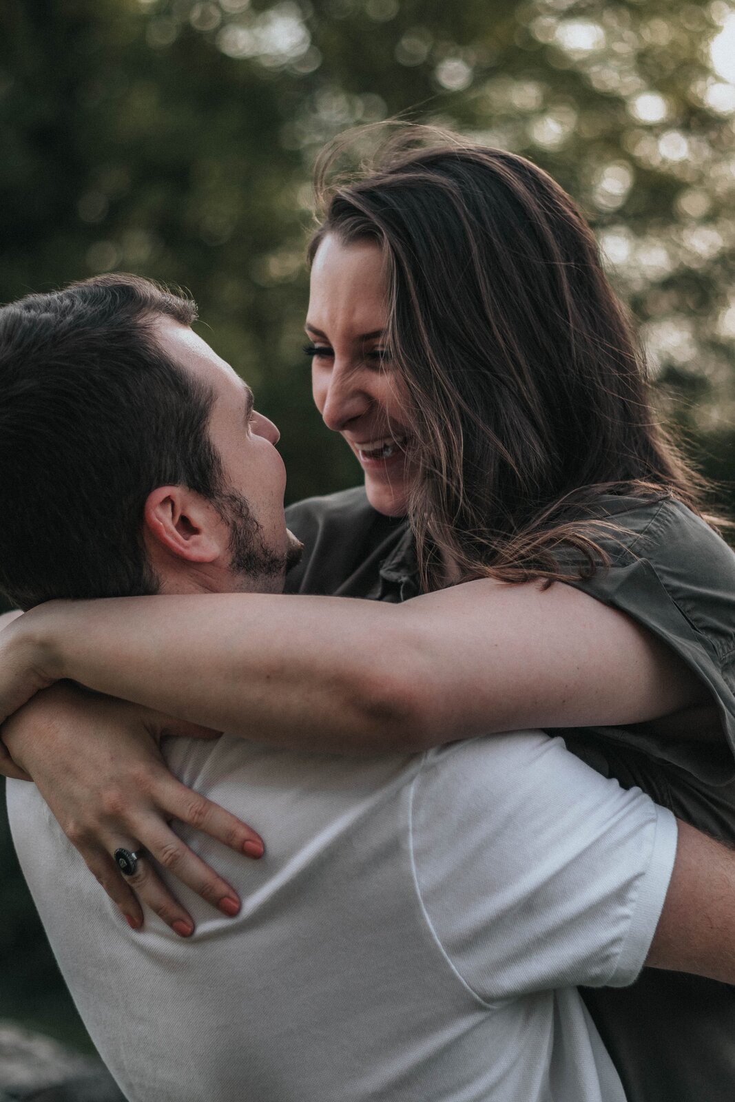 Zdjęcie przedstawia uśmiechniętą parę. Mężczyzna trzyma kobietę w pasie, a ona ma zarzucone ręce na jego szyi. Patrząc sobie w oczy i uśmiechają się szeroko. 