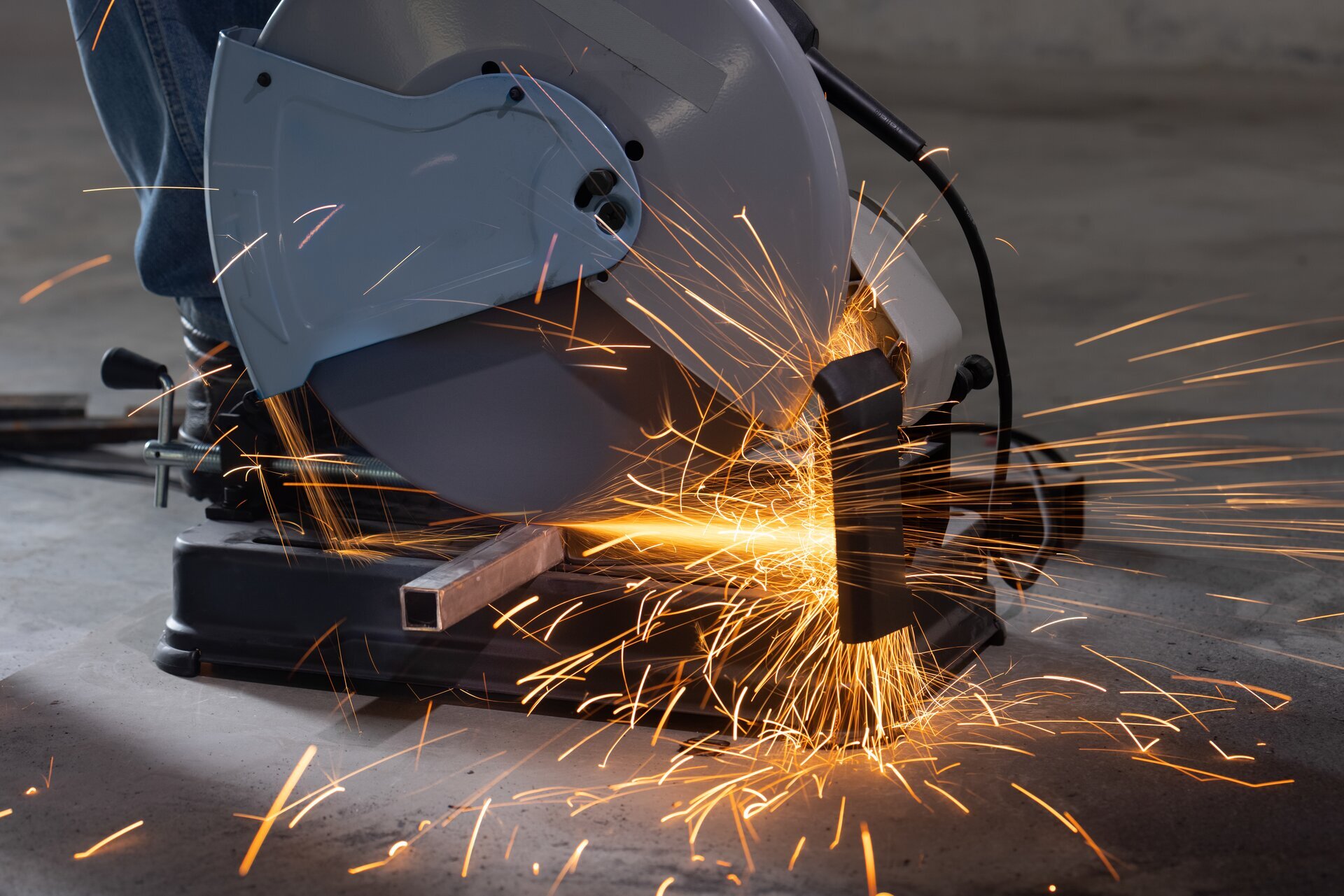 Zdjęcie przedstawia szlifierkę kątową, która przecina stalowy pręt o kwadratowy przekroju.