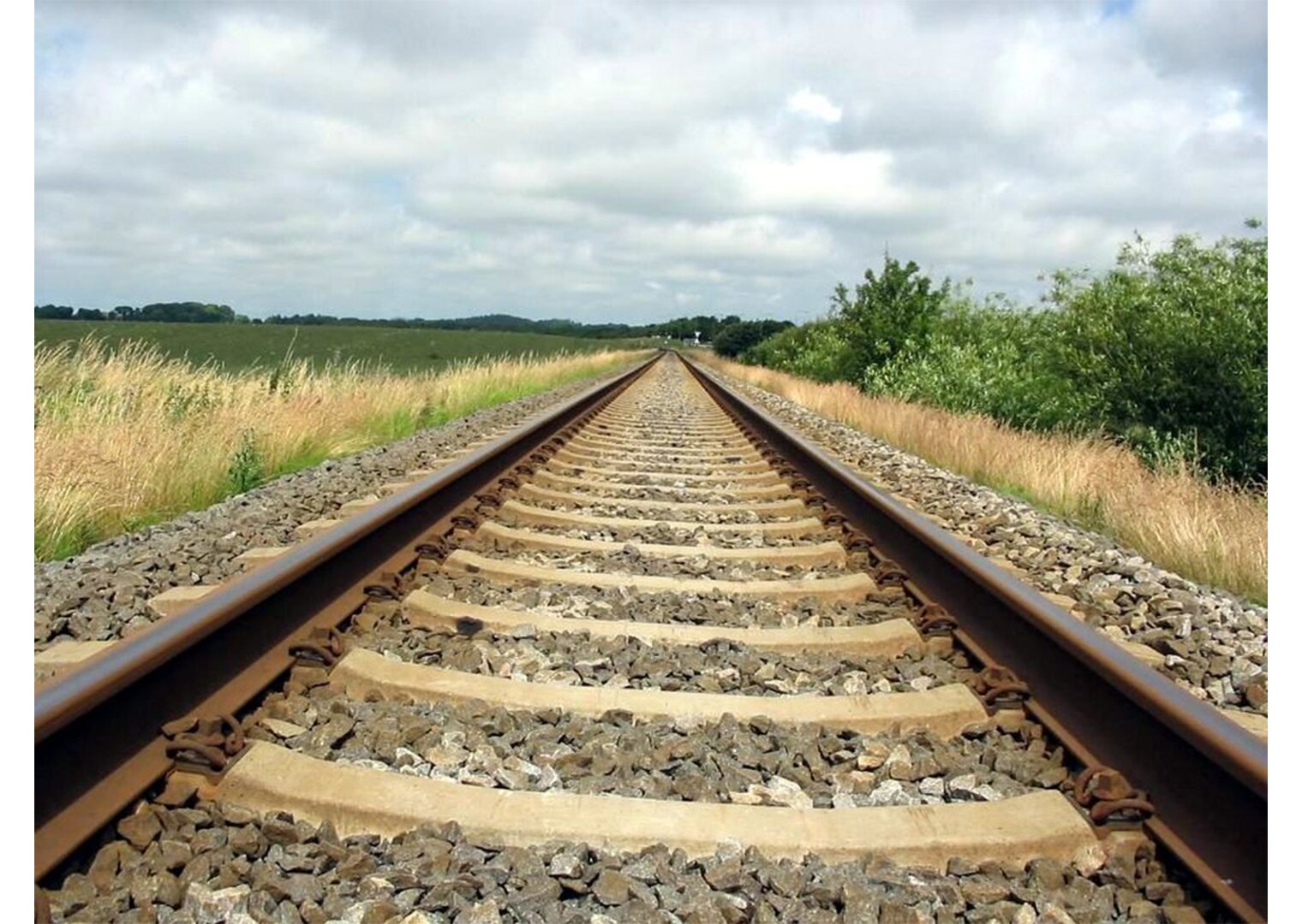  Zdjęcie przedstawia teren pozamiejski gdzie przebiega trasa kolejowa. Tory ułożone są na betonowych podporach oraz obsypane drobnymi kamieniami które, pochłaniają wibracje podczas przejazdu pociągu.