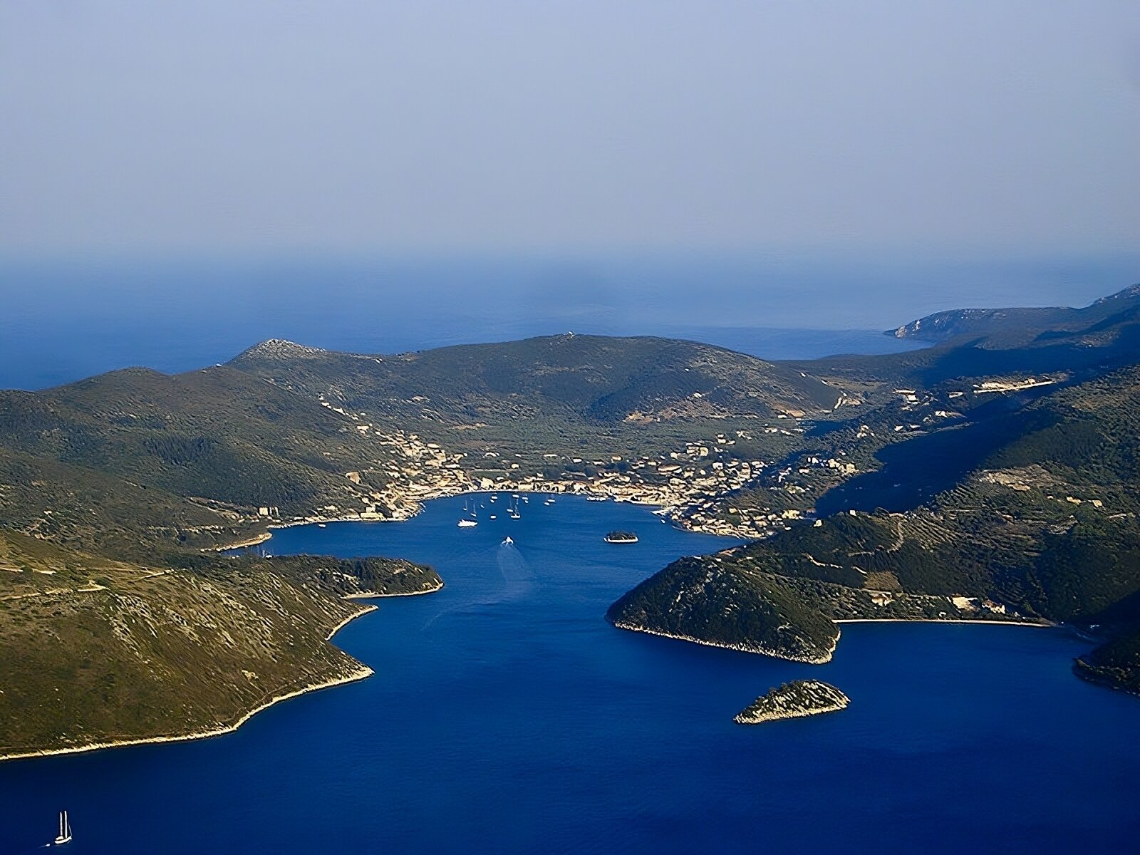 Na zdjęciu z lotu ptaka widać wyspę i otaczające ją morze. Na pierwszym planie znajduje się wąska zatoka, pływają po niej statki, a przy brzegu morza wyrasta miasto (centralnie na zdjęciu). Wyspa ma charakter górzysty, porośnięta jest skąpą roślinnością. 