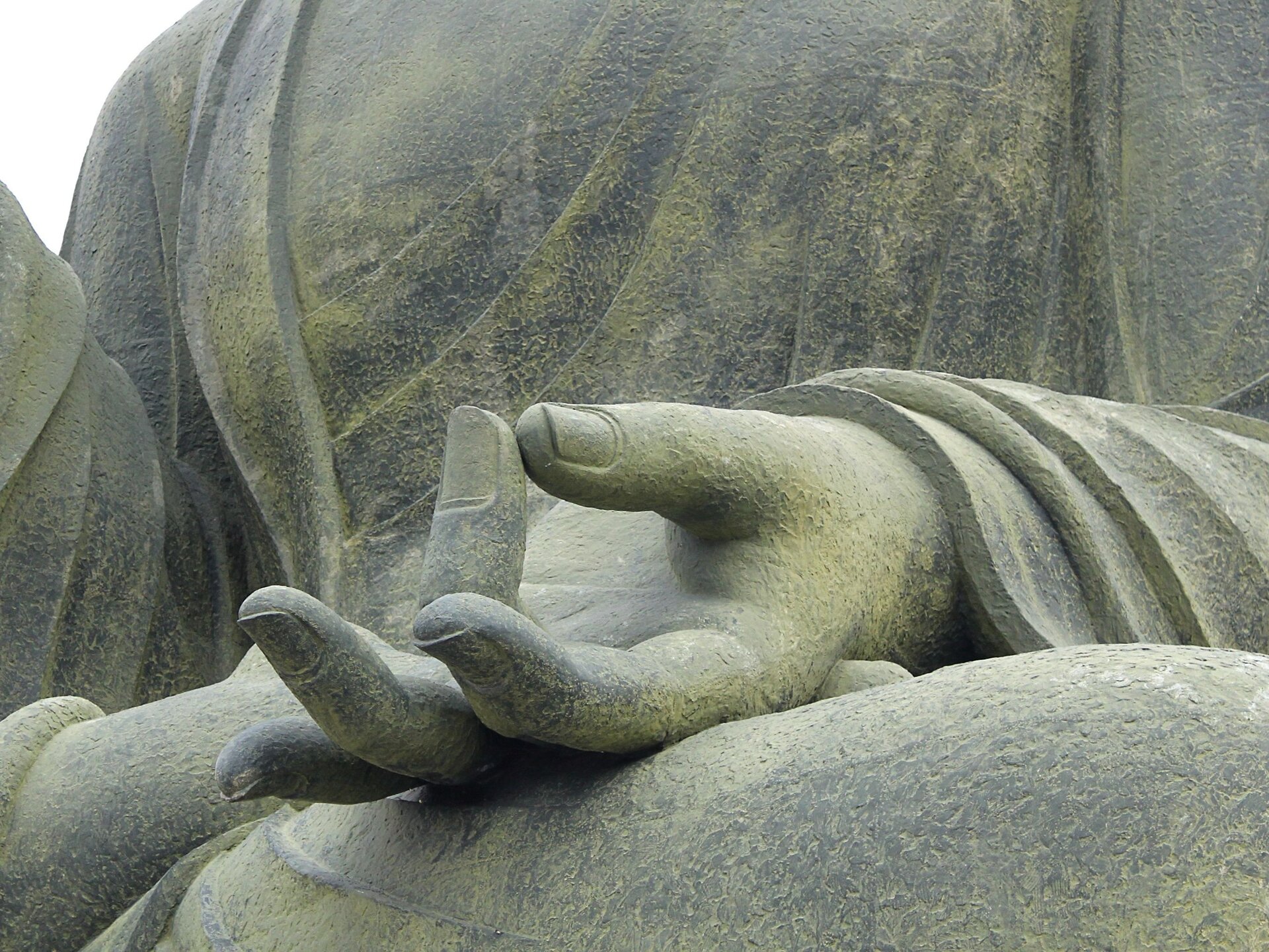 Fotografia przedstawia fragment rzeźby z kamienia. Jest to dłoń ułożona płasko, której palec serdeczny i kciuk lekko stykają się ze sobą.