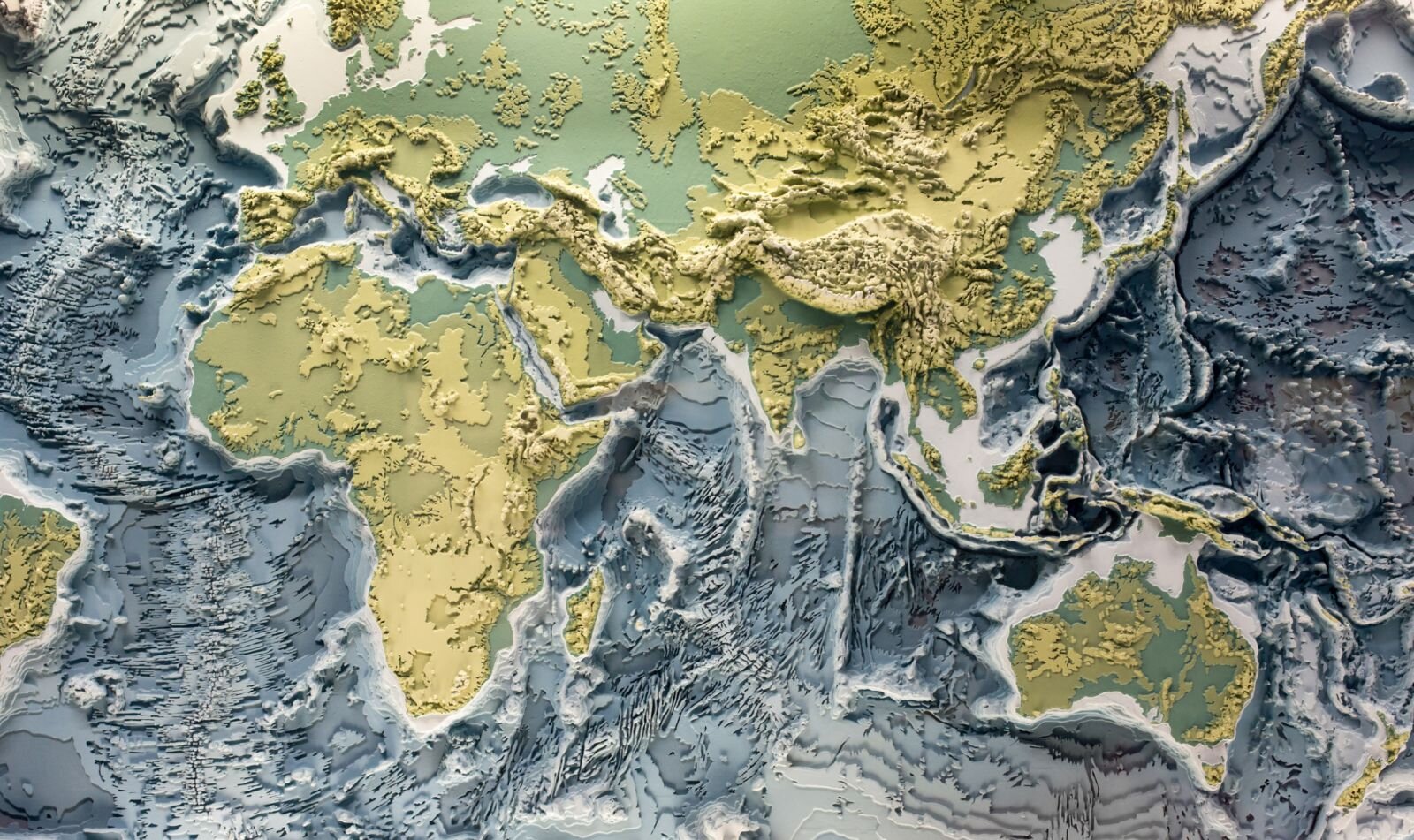 Zdjęcie przedstawia mapę, którą można dotykać, aby poznać różnice w ukształtowaniu terenu. Jest na niej część kontynentu Europy i Azji, Afryka i Australia, oraz morza i oceany, których głębokość też można zbadać dotykając palcami powierzchni.