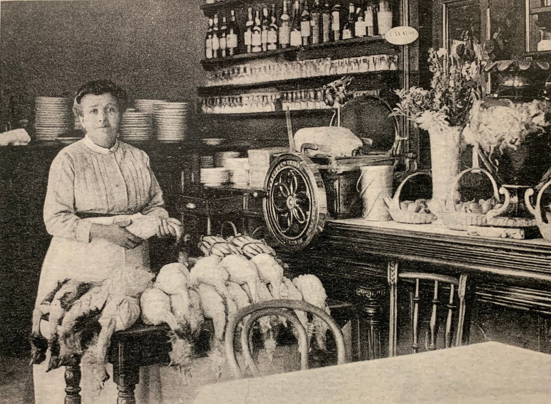Na zdjęciu widoczna jest Françoise Fayolle, znana jako Mère Fillioux, przygotowująca kurczaki w swojej restauracji w Lyonie około 1900 roku. Mère Fillioux była cenioną postacią w świecie kulinarnej Lyonu i słynęła z doskonałego przygotowywania tradycyjnych dań francuskich. Zdjęcie ukazuje ją w akcji, w otoczeniu kuchennych narzędzi i aromatycznych składników, podkreślając jej pasję i zaangażowanie w sztukę kulinarnej przyjemności.