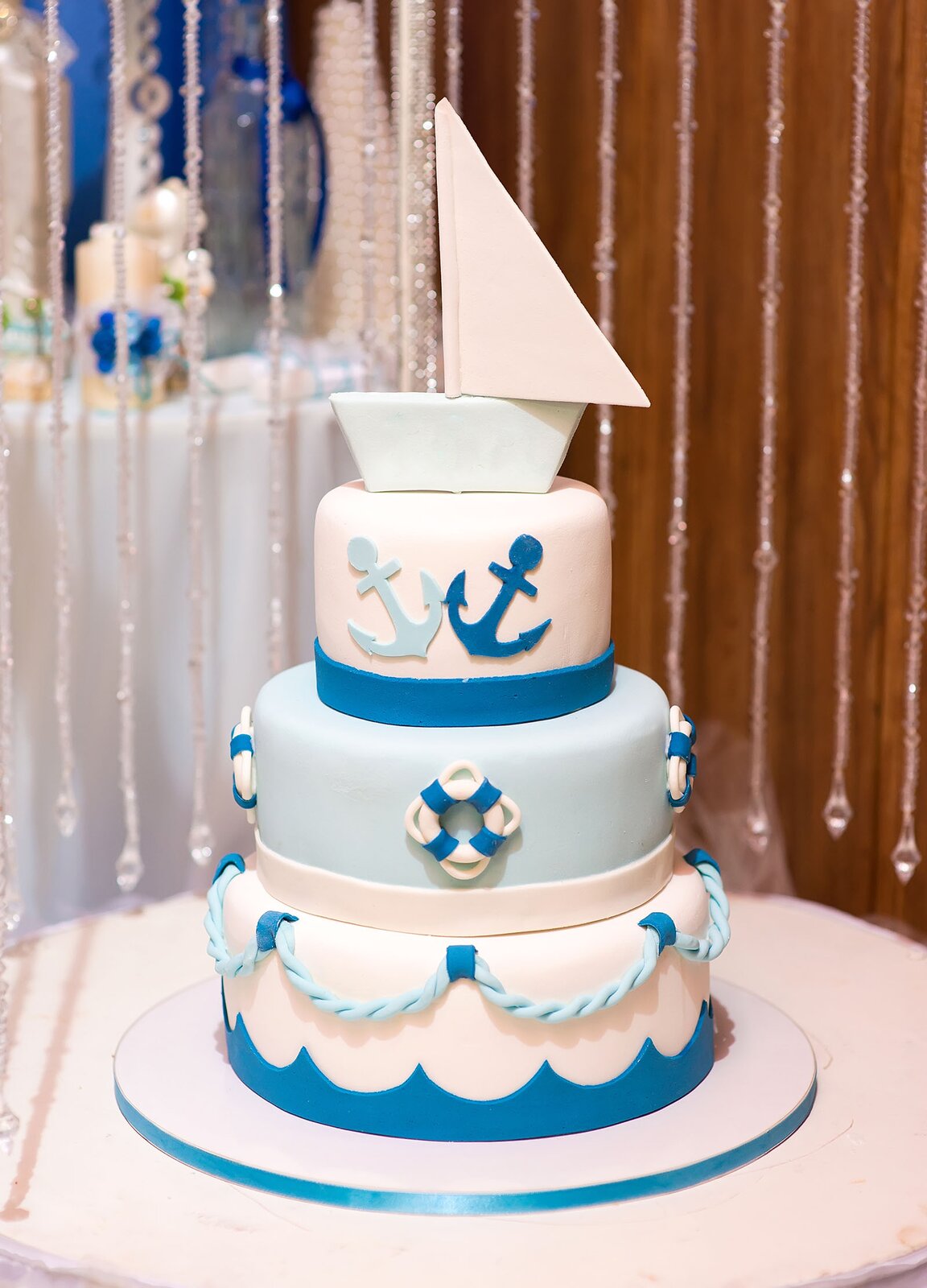 Zdjęcie przedstawia okrągły, trzypoziomowy tort w odcieniach niebieskiego i białego. Każdy z poziomów jest udekorowany elementami związanymi z żeglowaniem. Dookoła najniższej warstwy umieszczono niebieskie fale a nad nimi sznur. Drugi poziom udekorowano kołami ratunkowymi, a trzeci kotwicami. Na samej górze ustawiono żaglówkę.