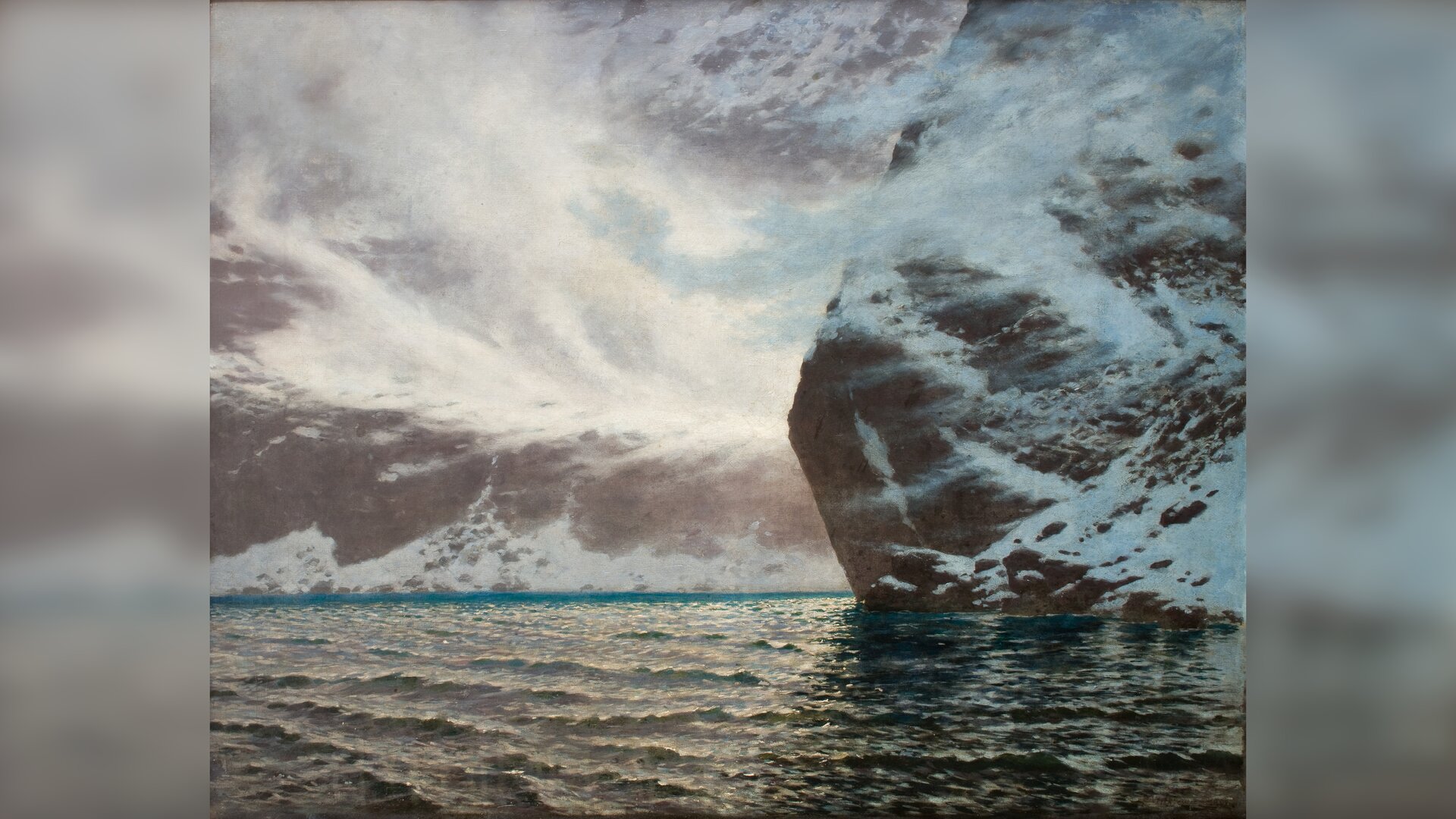 Ilustracja przedstawia górski pejzaż. Na pierwszym planie ukazana jest tafla lekko falującej wody. Po prawej stronie wyrasta z wody wysoka, ośnieżona skała. W tle zachmurzone niebo.