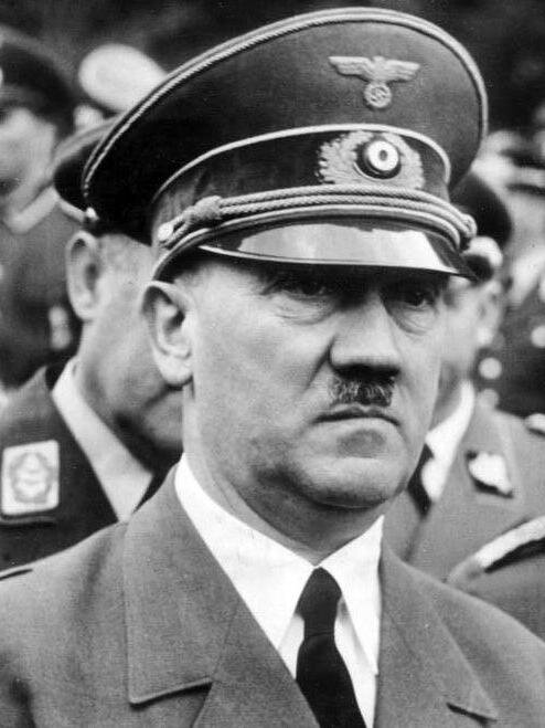 Zdjęcie przedstawia twarz Adolfa Hitlera. Mężczyzna ma owalną twarz i mały wąs pod nosem. Jest w mundurze i wojskowej czapce.
