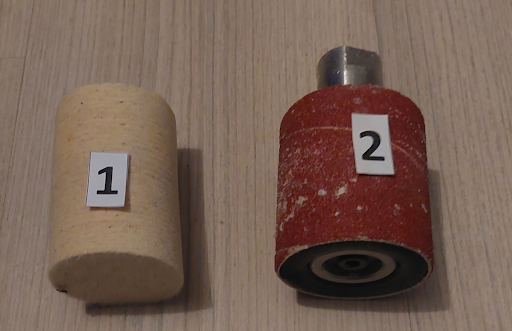 Zdjęcie przedstawiające dwa wałki osadzone na metalowych trzpieniach. Wałek jeden jest wykonany z materiału przypominającego gąbkę, a wałek dwa jest pokryty papierem ściernym.