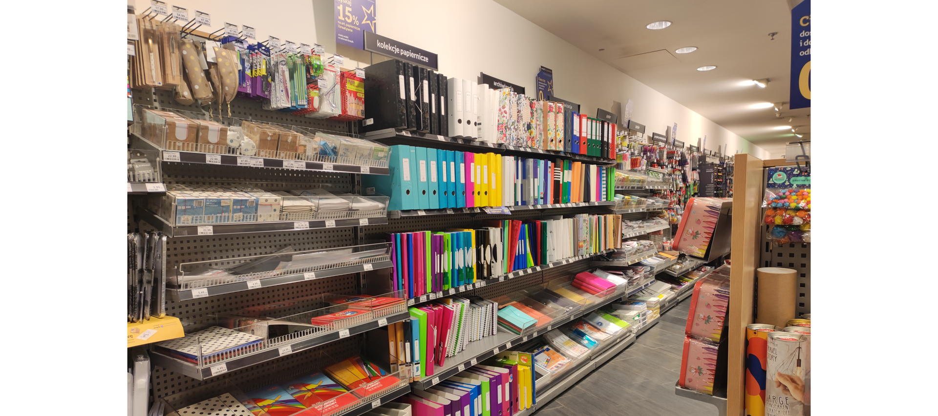 Zdjęcie przedstawia wnętrze sklepu z artykułami papierniczymi i biurowymi. Widoczne są regały z wyeksponowanymi artykułami.