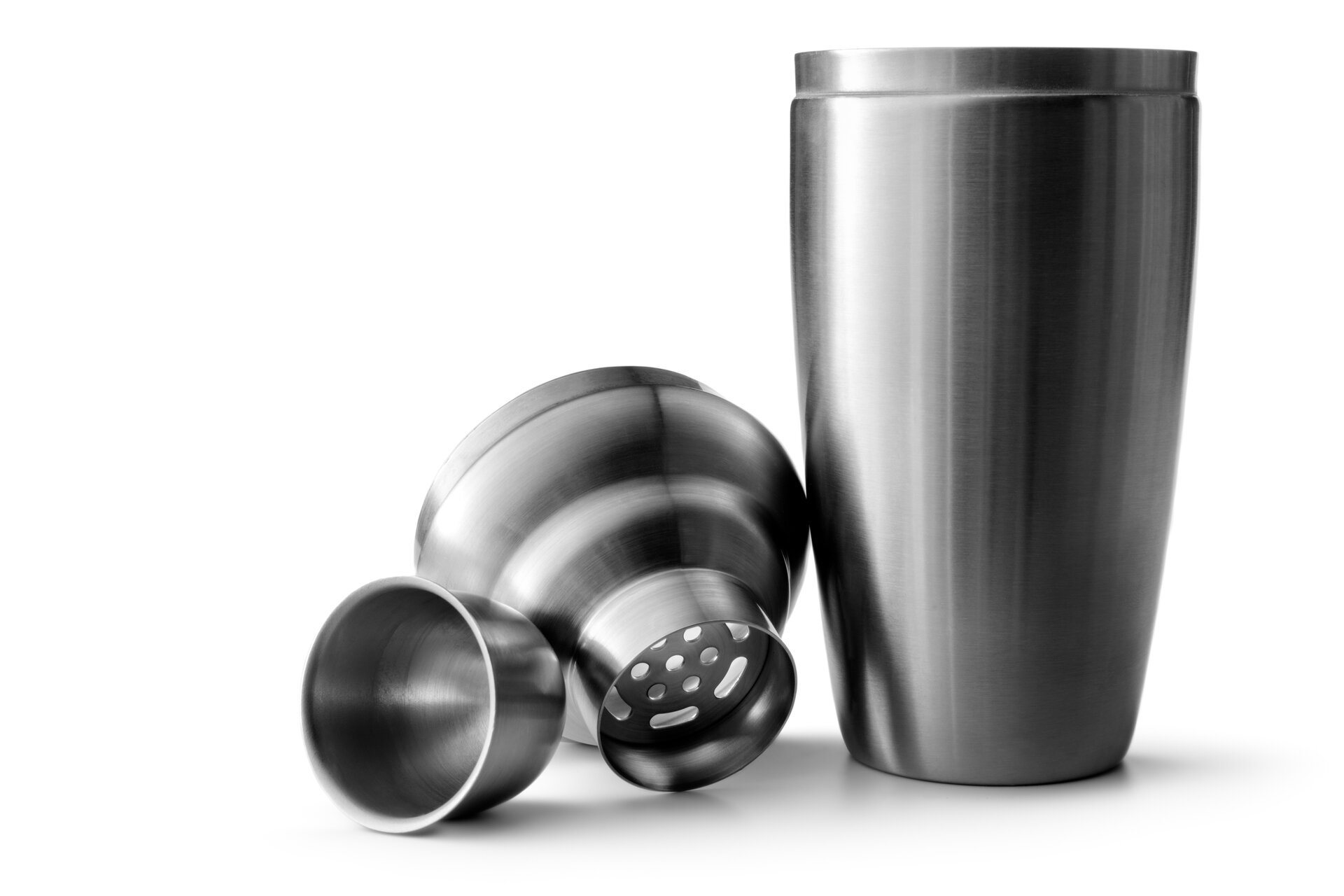 Zdjęcie przedstawia shaker zbudowany z metalowego kubka, wieczka z sitkiem i zakrętki. Wieczko i zakrętka leżą obok metalowego kubka.