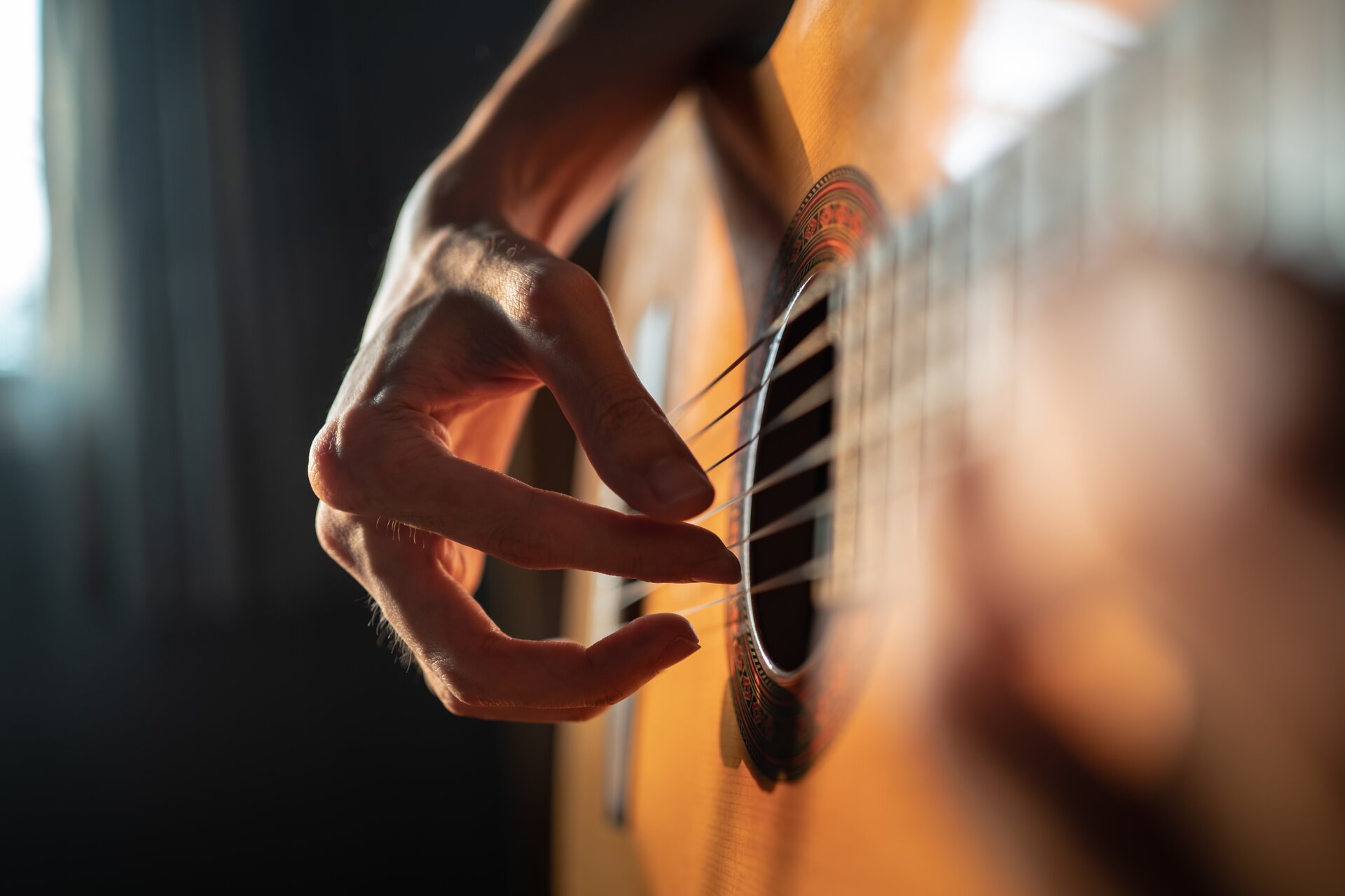 Fotografia przedstawia prawą rękę człowieka ułożoną na strunach nad otworem rezonansowym gitary. Czubki palców lekko dotykają strun, nadgarstek jest podniesiony do góry.