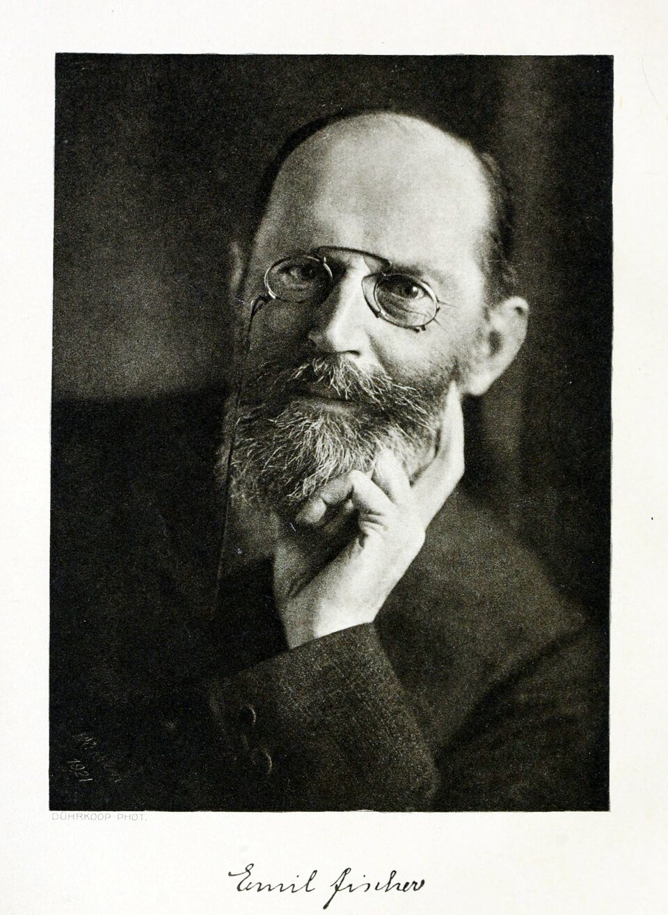 Na zdjęciu jest mężczyzna z brodą i w okularach. Ma wysokie czoło, łysieje. Podbródek wspiera na lewej dłoni. Jest lekko uśmiechnięty.