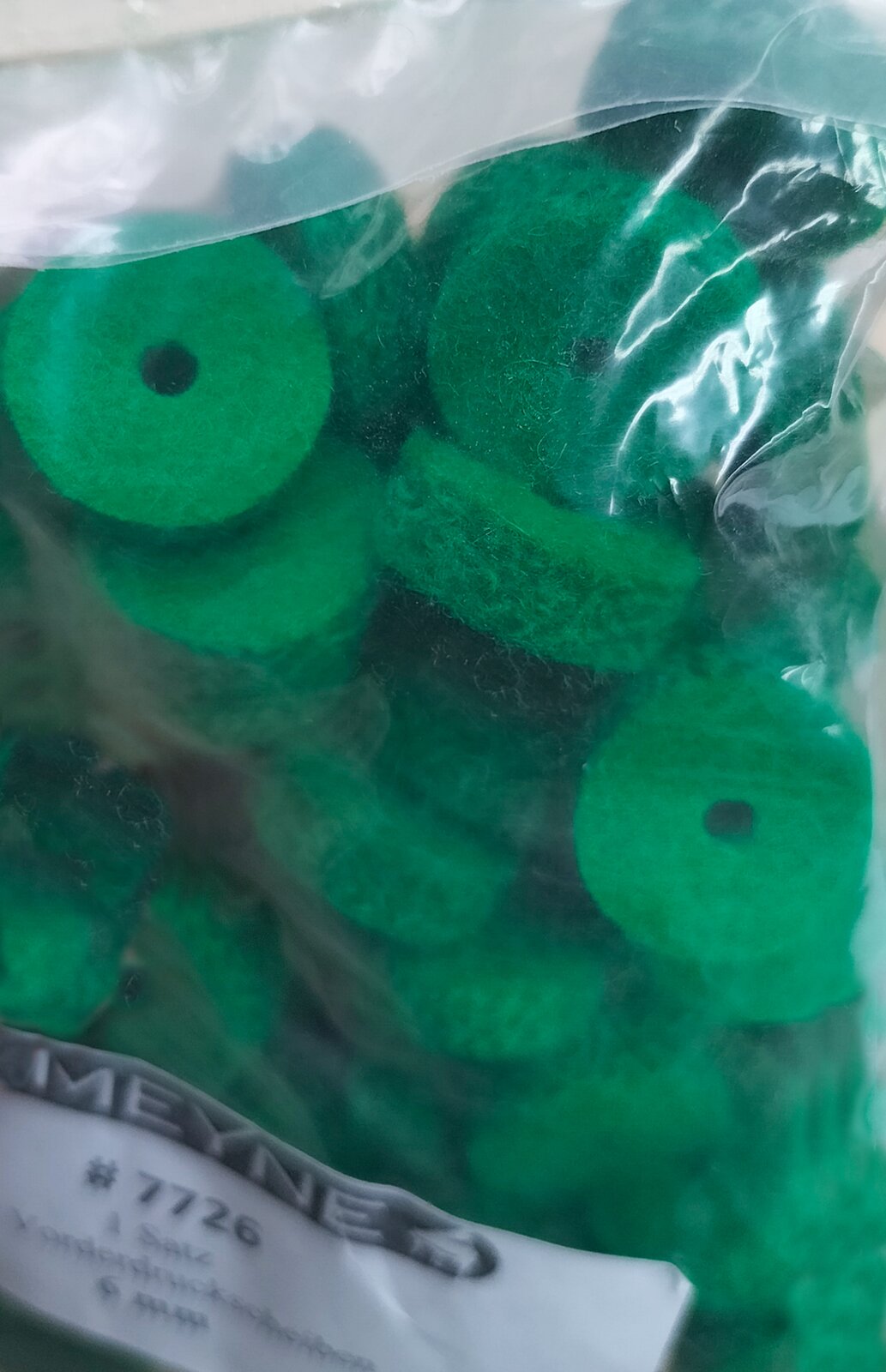 Zdjęcie przedstawia podkładki pod klawisze na sztyftach płaskich wykonane z filcu tkanego w kolorze zielonym, w przeźroczystym foliowym opakowaniu z białą etykietą z czarnymi napisami.