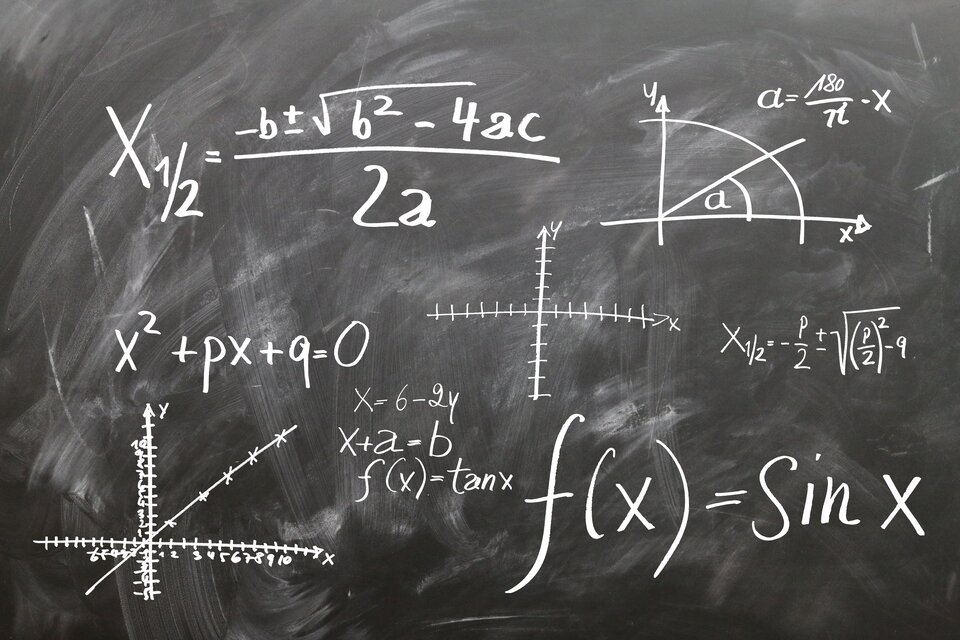 Ilustracja przedstawia tablicę szkolną z zapisanymi na niej kredą różnorodnymi równaniami, działaniami, symbolami matematycznymi.