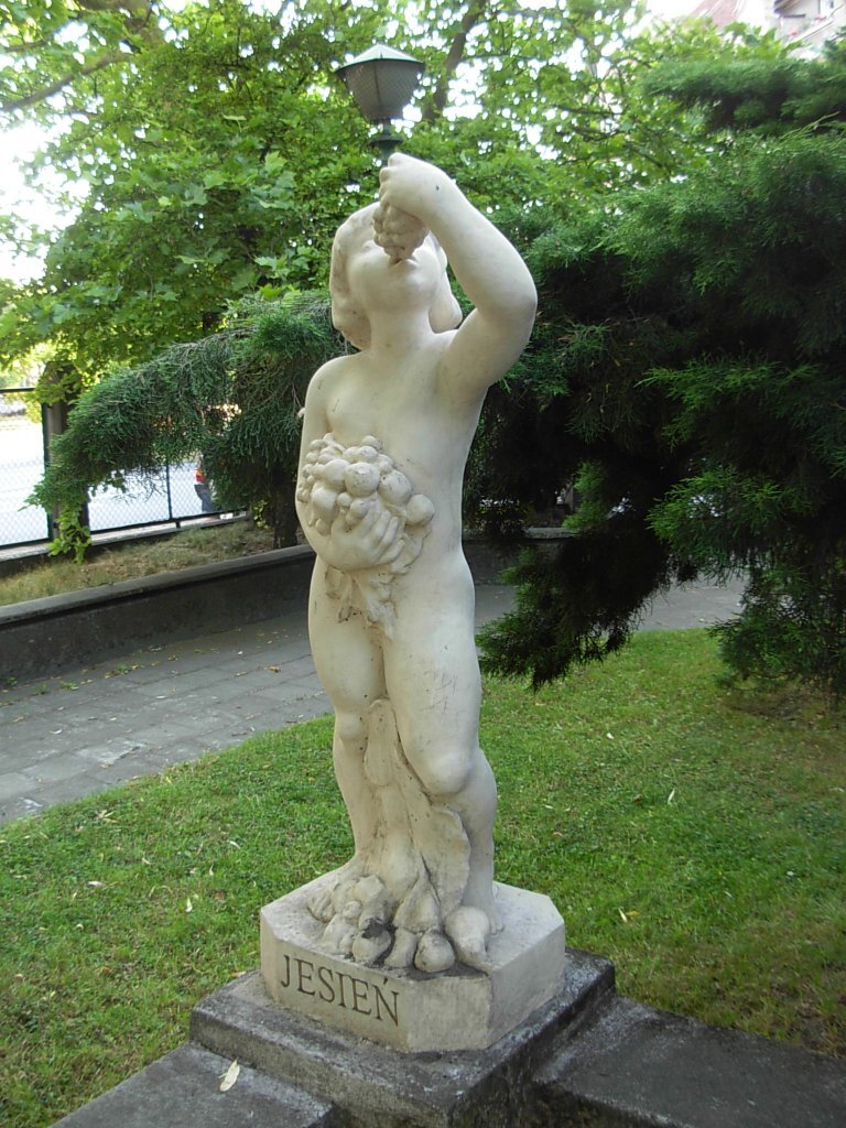 Zdjęcie przedstawia rzeźbę. Przedstawia nagie dziecko, które je winogrona. Na postumencie rzeźby znajduje się napis: Jesień.