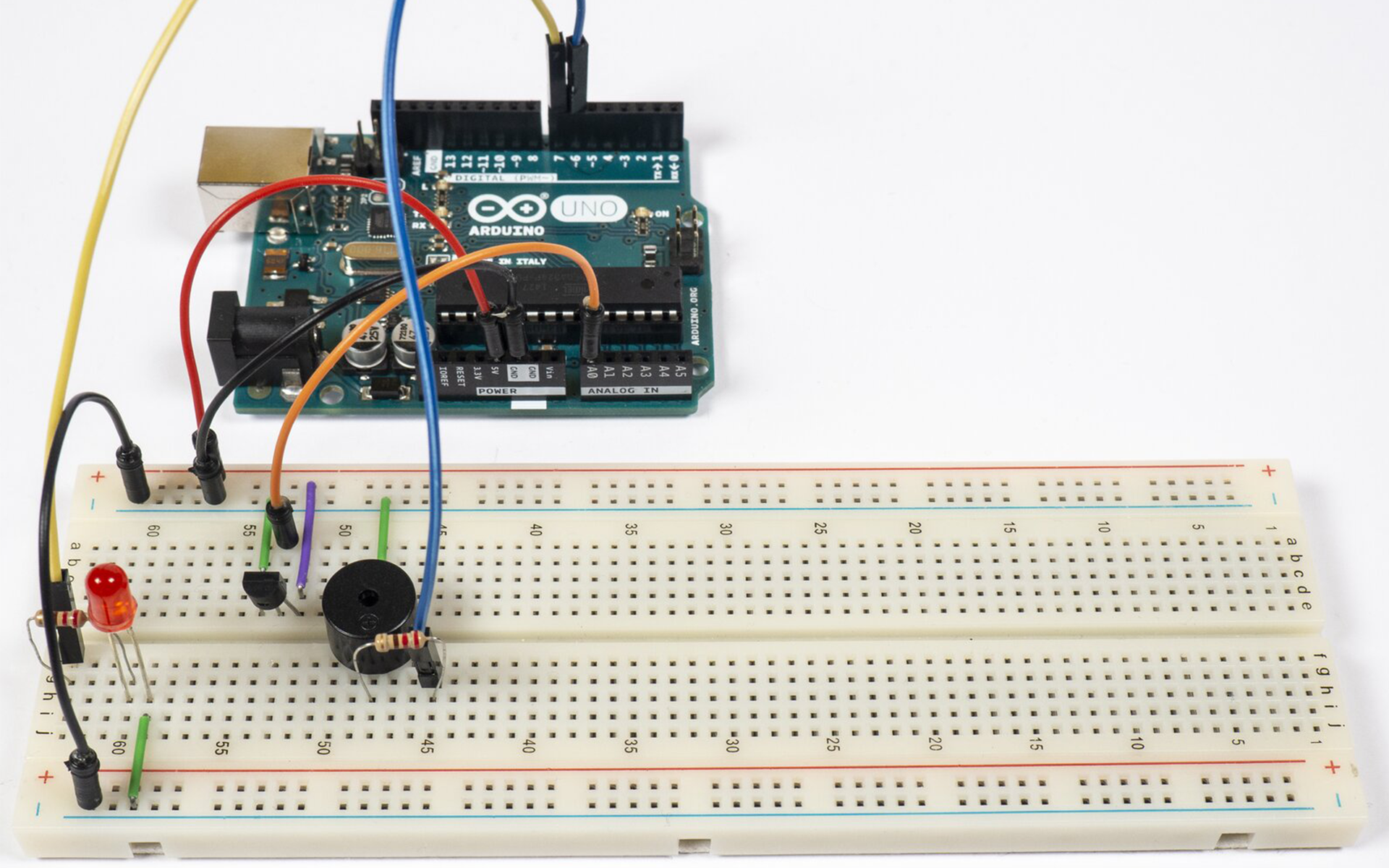Zdjęcie przedstawia połączenia pomiędzy arduino uno, a płytką stykową. Na płytce znajduje się termometr (względem wycięcia w obudowie) podłączony jest prawą nóżką do uziemienia, lewą do +5V a środkową do pinu A0 arduino. Pin 5V podłączony jest do +5V płytki, a GND podłączone jest do uziemienia. Uziemienie górnej szyny jak i dolnej na płytce stykowej jest połączone. Podłączona jest także LED, jedną nóżką do uziemienia, drugą zaś poprzez rezystor do pinu 7 arduino. Po środku płytki zamontowany jest brzęczyk, który poprzez rezystor łączy się z pinem 6 arduino, a drugą nóżką do uziemienia.
