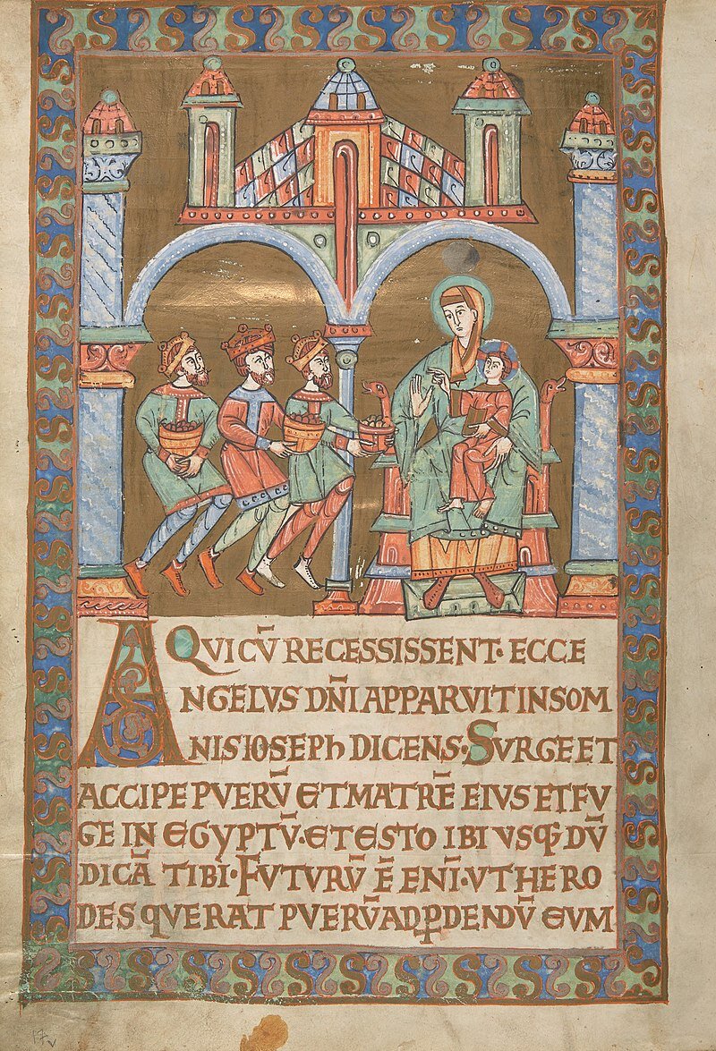 Na zdjęciu znajduje się zdobiona strona ręcznie przepisywanej księgi. Ilustracja przedstawia trzech króli, którzy przybyli do Maryi i małego Jezusa. W dolnej części znajdują się tekst po łacinie. Cała strona wypełniona jest kolorowymi wzorami. 