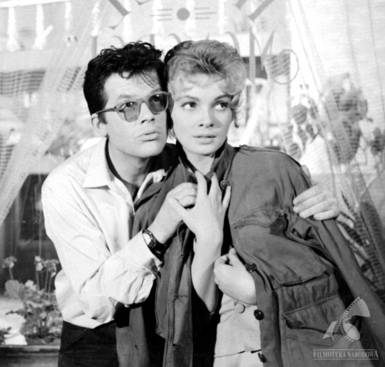 Zdjęcie przedstawia parę ludzi przytulonych policzkami do siebie. Mężczyzna obejmuje kobietę lewą ręką.