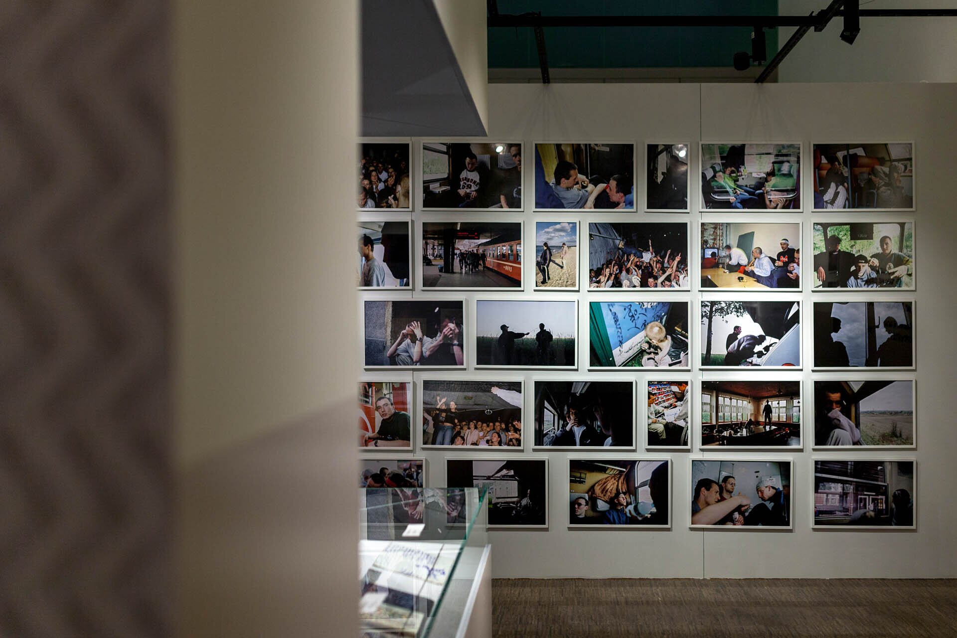 Fotografia przedstawia ścianę, na której uchwycono liczne fotografie raperów. Są one umieszczone w prostokątnych ramkach. Większość fotografii jest pozioma o takich samych rozmiarach. Fotografie pionowe są węższe, ale ich wysokość jest taka sama jak fotografii pionowych. Kolory są zgaszone, a odcienie głównie zimne. Fotografie przedstawiają sceny z koncertów, spotkania z fanami, sceny z podróży. Tło stanowią brązowa podłoga oraz kremowa ściana.