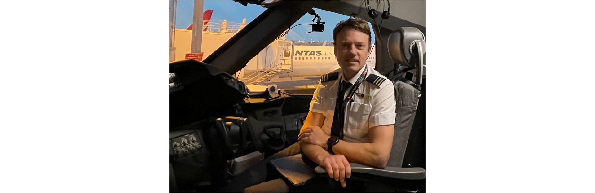 Zdjęcie przedstawia mężczyznę, pilota. Mężczyzna siedzi w fotelu w kokpicie samolotu. Ubrany jest w mundur pilota.