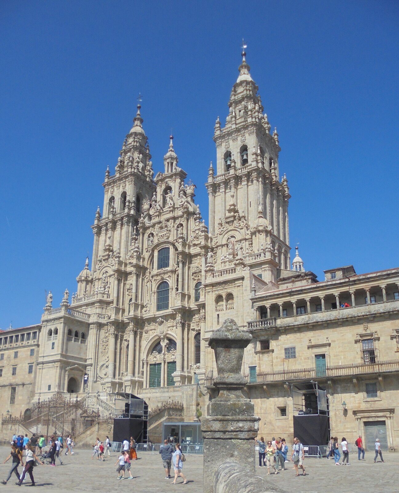 Ilustracja przedstawia fasadę Katedry w Santiago de Compostela w Hiszpanii. Monumentalna fasada, przebudowana w baroku jest flankowana dwiema wieżami na planie kwadratu. Przed katedrą znajduje się kilka ciągów szerokich schodów, które prowadzą do wejścia do górnego kościoła. Reprezentacyjna fasada oraz schody są bogato dekorowane. Przed katedrą znajduje się ogromny plac po którym spacerują ludzie. Barokową fasadę del Obradoiro, nazwaną od placu Plaza do Obradoiro, wykonał Fernando de Casas y Nóvoa, w latach 1738-1749. Charakteryzuje ją dekoracyjne i ikonograficzne bogactwo (m.in. rzeźby przedstawiające postaci Św. Jakuba, jego dwóch uczniów oraz scenę związaną z cudownym odkryciem ich grobów). Po obu stronach usytuowane są masywne wieże na planie kwadratu. Pielgrzymkowego charakteru nadają dwa rzędy schodów.