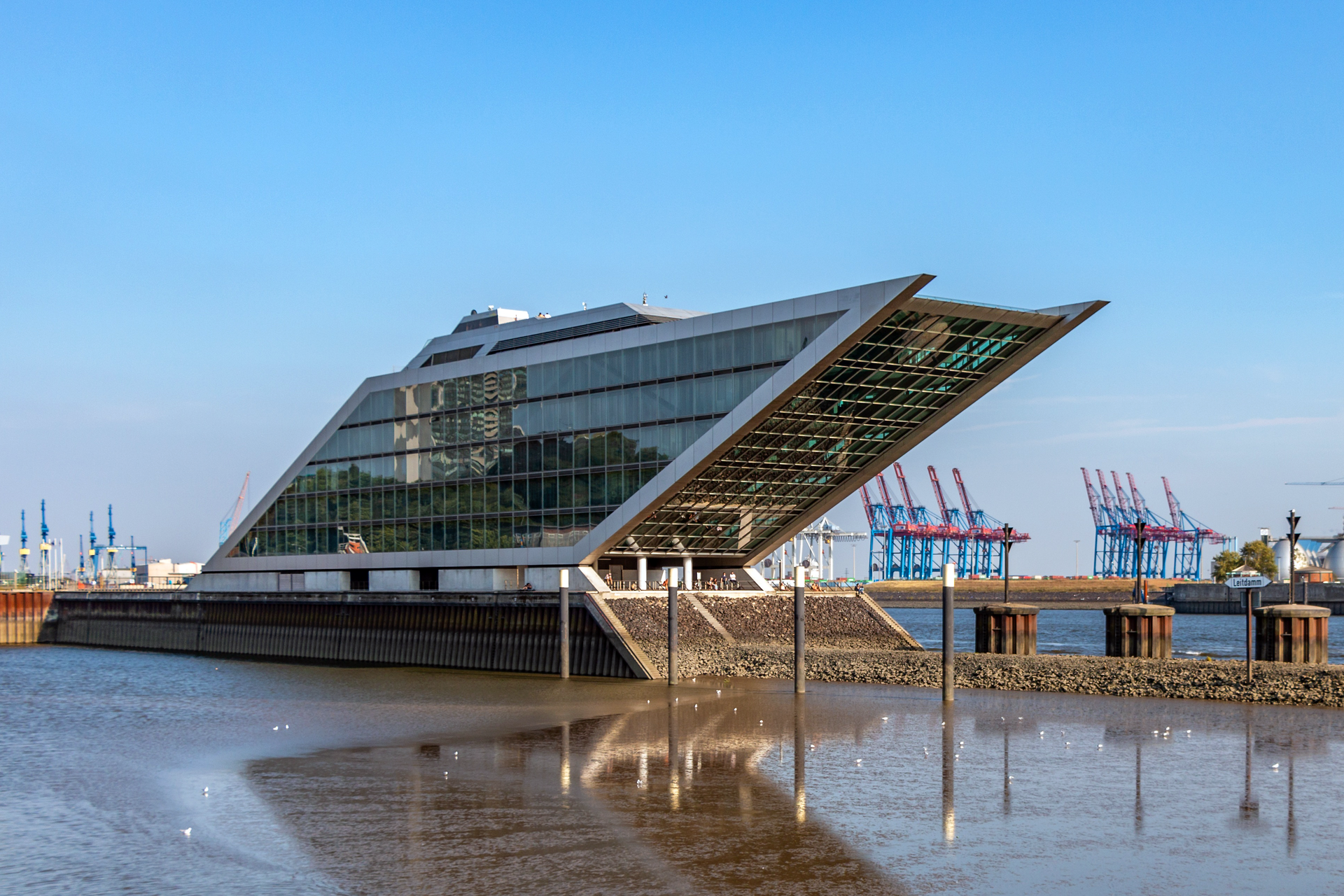 Ilustracja przedstawia szklany budynek w kształcie równoległoboku.