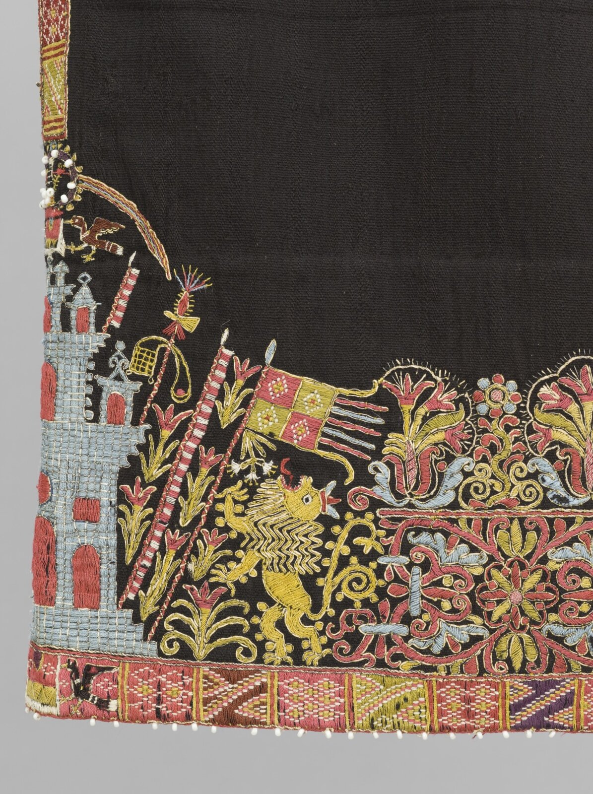 Ilustracja przedstawia ciemny materiał ozdobiony kolorowym haftem.