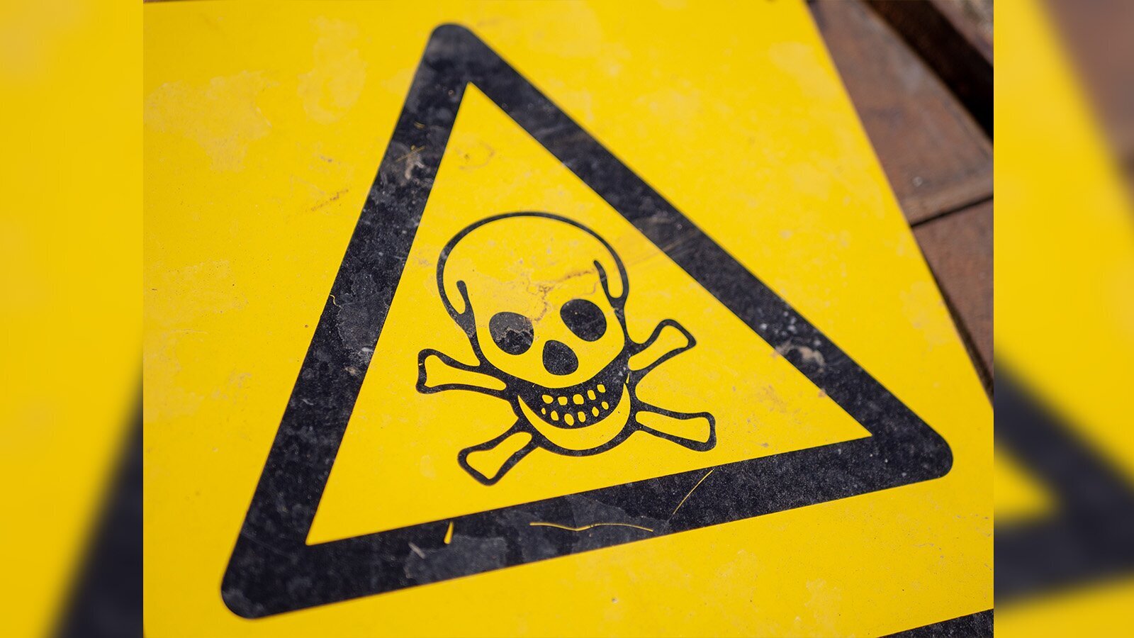 Zdjęcie przedstawia tabliczkę ostrzegawczą w kolorze żółtym, na której widoczny jest czarny trójkąt równoramienny, w który wpisana została ludzka czaszka ze skrzyżowanymi piszczelami.