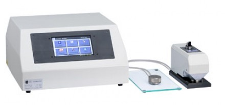 Grafika prezentuje aparat Bendstena. Urządzenie składa się z trzech elementów: po lewej stronie widoczna jest skrzynka wyposażona w panel z przyciskami, do niej podłączona jest szklana podstawka pod próbki oraz biało‑szare, niewielkie urządzenie.