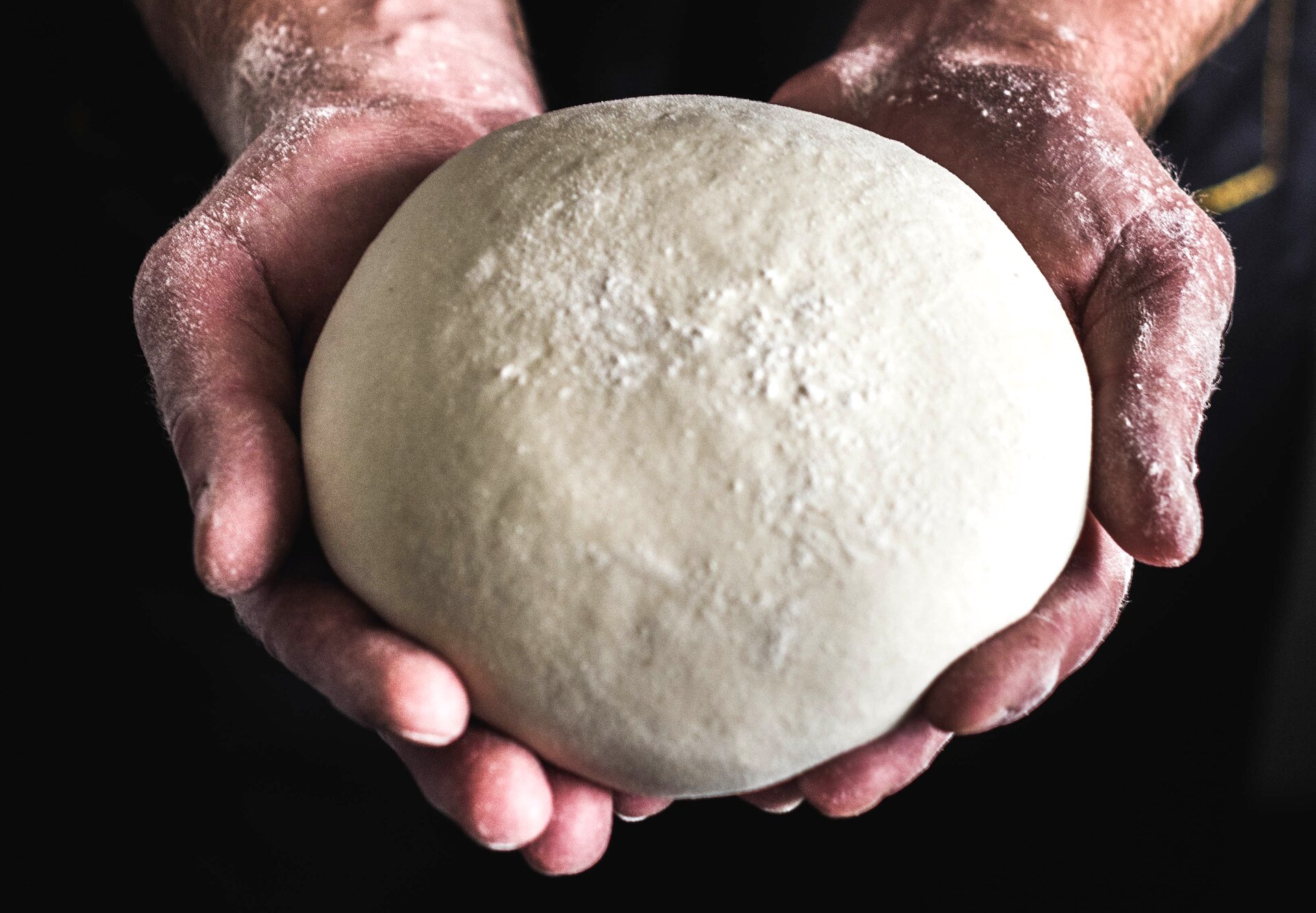 Zdjęcie przedstawia kulę ciasta, oprószoną mąką, trzymaną w otwartych dłoniach.