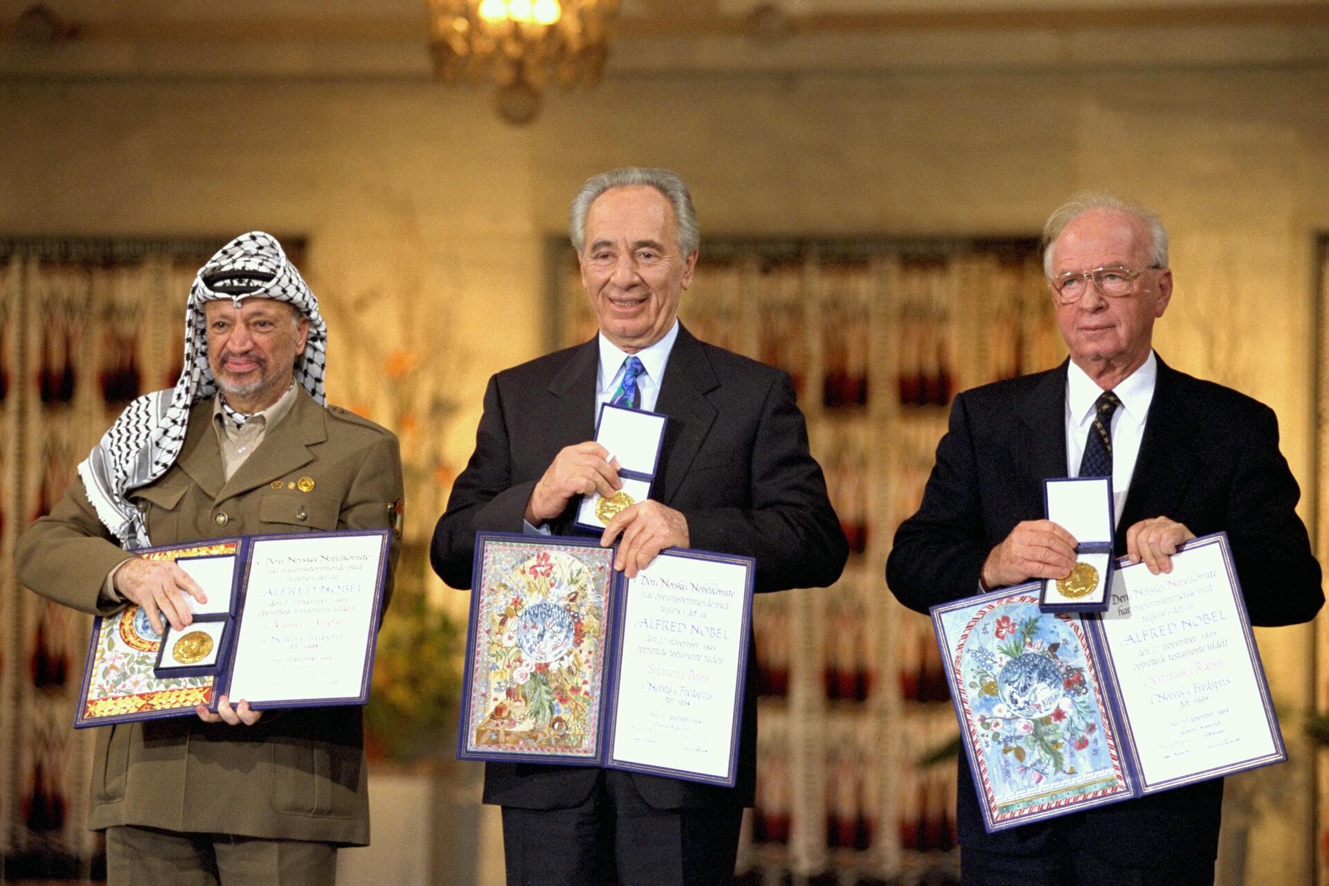 Na zdjęciu trzej mężczyźni, jeden w mundurze i chuście na głowie, dwaj w garniturach. Pokazują medale i dyplomy.