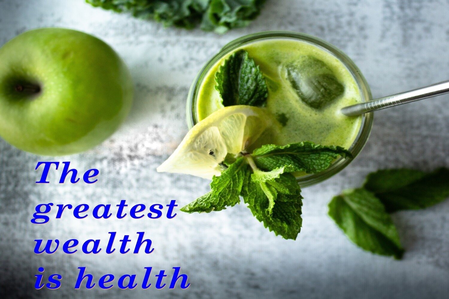 Zdjęcie przedstawia szary blat, w ujęciu z góry. Na blacie po lewej stronie widoczne jest zielone jabłko, a w środku widoczna jest szklanka, wypełniona jasnozielonym, lekko spienionym płynem, w którym pływa kostka lodu i włożone są: plaster cytryny, gałązka mięty oraz metalowa słomka. Obok szklanki leżą na blacie pojedyncze listki mięty. W lewym dolnym rogu widoczny jest ciemnoniebieski napis w języku angielskim: The greatest wealth is health.
