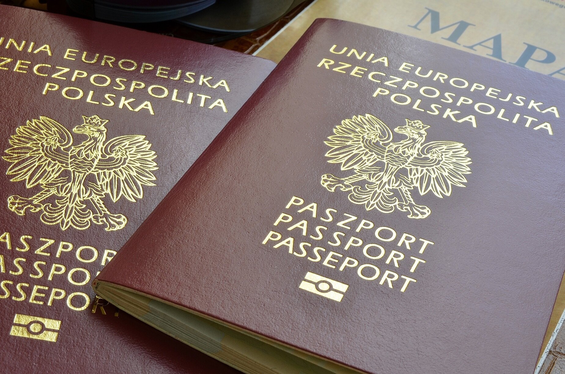 Zdjęcie przedstawia książeczki paszportowe ułożone na stole. Na książeczce widnieje godło polskie oraz napisy: Unia Europejska Rzeczpospolita Polska, Paszport, Passport, Passeport.