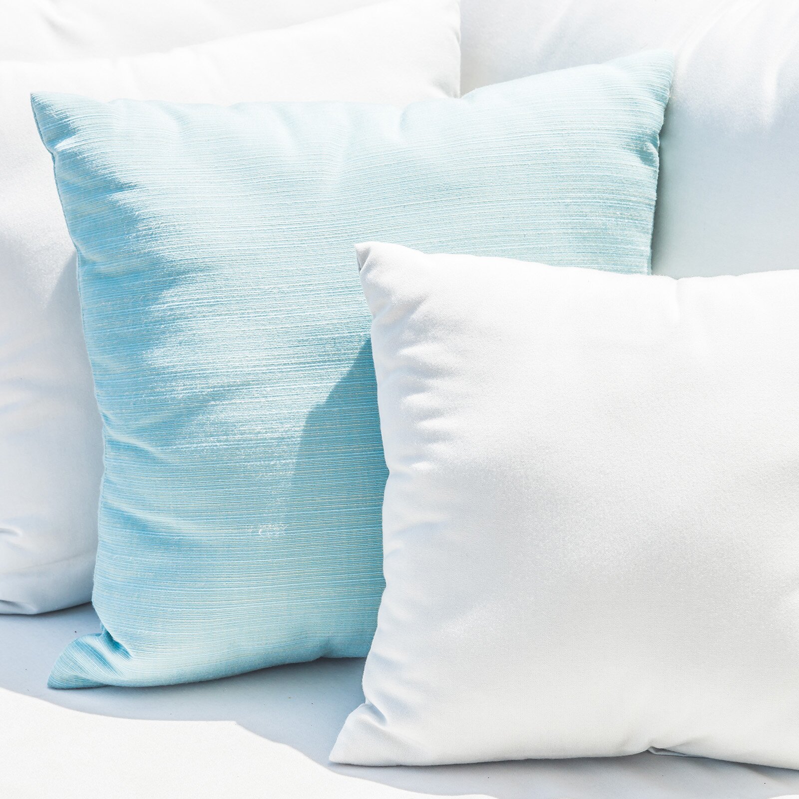 Zdjęcie przedstawia trzy poduszki ustawione jedna obok drugiej. Dwie poduszki są białe a jedna jasno niebieska.