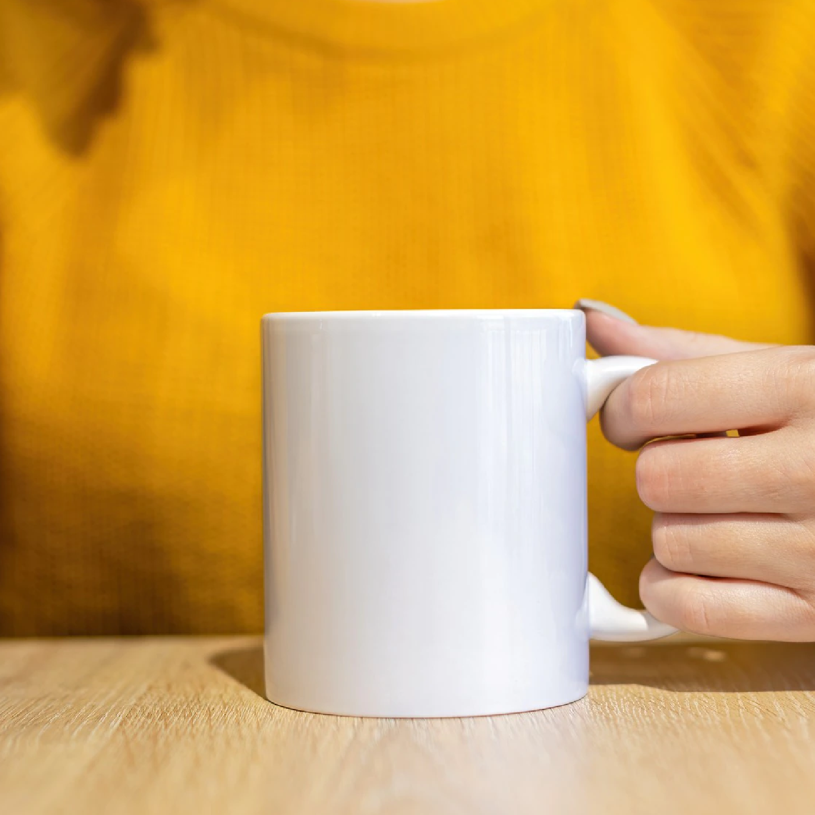 Zdjęcie przedstawia biały kubek, trzymany za ucho damską dłonią. 