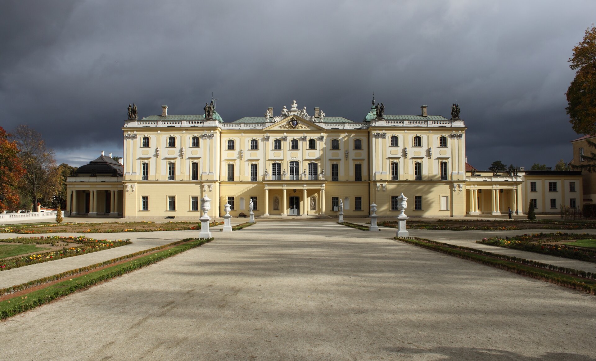 Fotografia przedstawia budynek o żółto‑białej elewacji. Konstrukcję budynku można podzielić na trzy części - dwa skrajne skrzydła oparte o kolumnadę, oraz budynek główny składający się z centralnej części oraz dwóch sąsiadująch z nim dobudówek. Budynek ma dwa piętra - pierwsze jak i drugie piętro posiadają taką samą ilość okien - po trzynaście sztuk. Okna rozłożone są równomiernie, ale te znajdujące się na drugim piętrze są mniejsze od tych na piętrze pierwszym. Wejście do budynku jest na parterze - po obu stornach drewnianych drzwi umieszczono dwie figury. Na parterze są również trzy blendy - czyli  ślepe otwory użyte jako element dekoracyjny. Do budynku prowadzi szeroka ścieżka, przy której ustawiono figury o kształcie pucharów. 